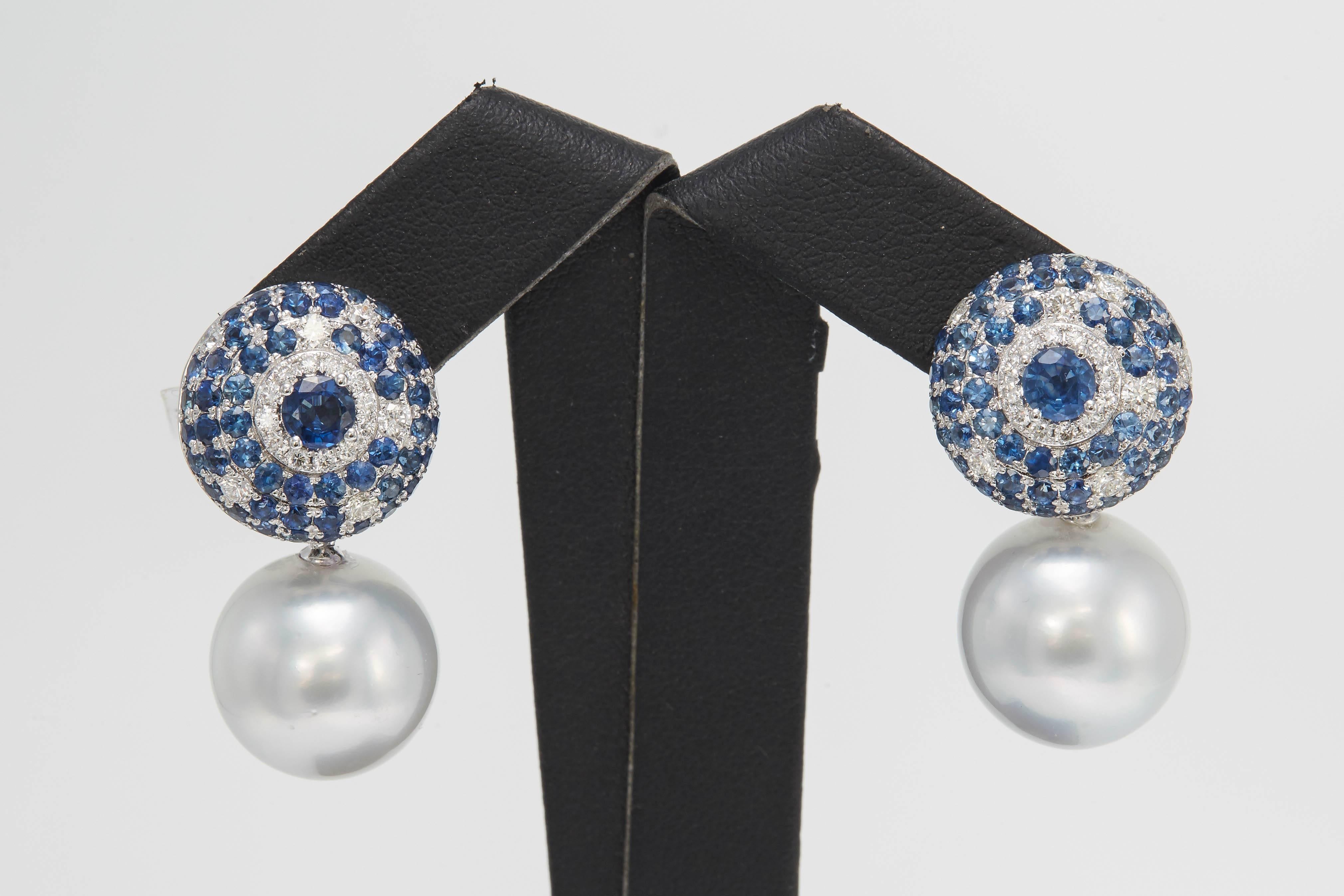 18K White gold earrings featuring two South Sea Pearls measuring 14-15 mm flanked with blue Sapphires weighing 4.90 carats and diamonds weighing 0.63 carats. Color G-H Clarity SI