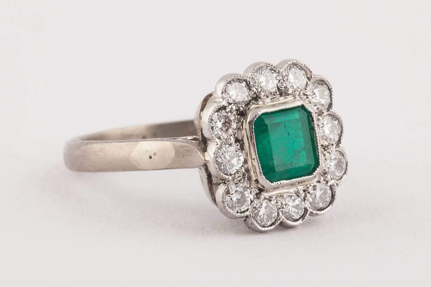 A beautiful square cut emerald and diamond cluster ring set with a vivid green emerald, surrounded by twelve bright diamonds, in millegrain setting, mounted in 18k white gold.

Mid 20th century. Marked 18ct.

Size 5 1/2.

Ring box illustrated is for
