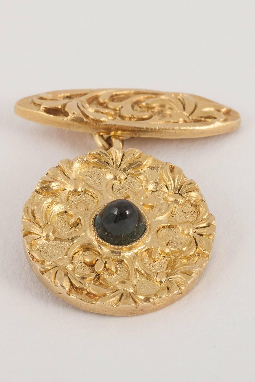 A single sided circular pair of French made, cufflinks,carved floral decoration of flowers, with a cabochon shaped sapphire centre,on chain links to a similarly carved long oval connection.C,1900