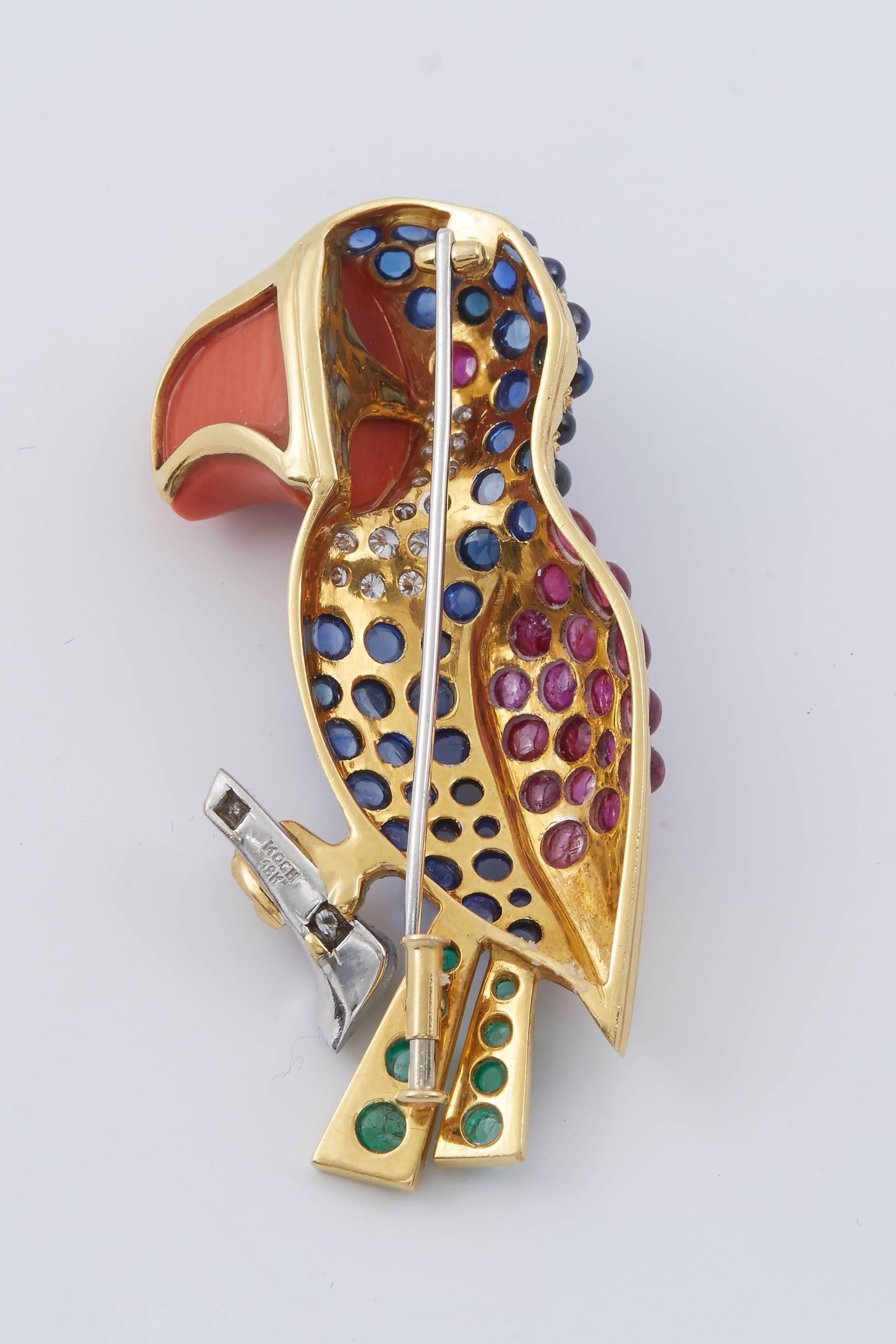 This beautiful 18k yellow gold bird brooch featuring cabochon 45 sapphire, 19 rubies, 8 emerald, 16 round cut diamonds and coral. 
The eye set centrally with a cabochon ruby, with diamond accents to either side, the body set throughout with cabochon