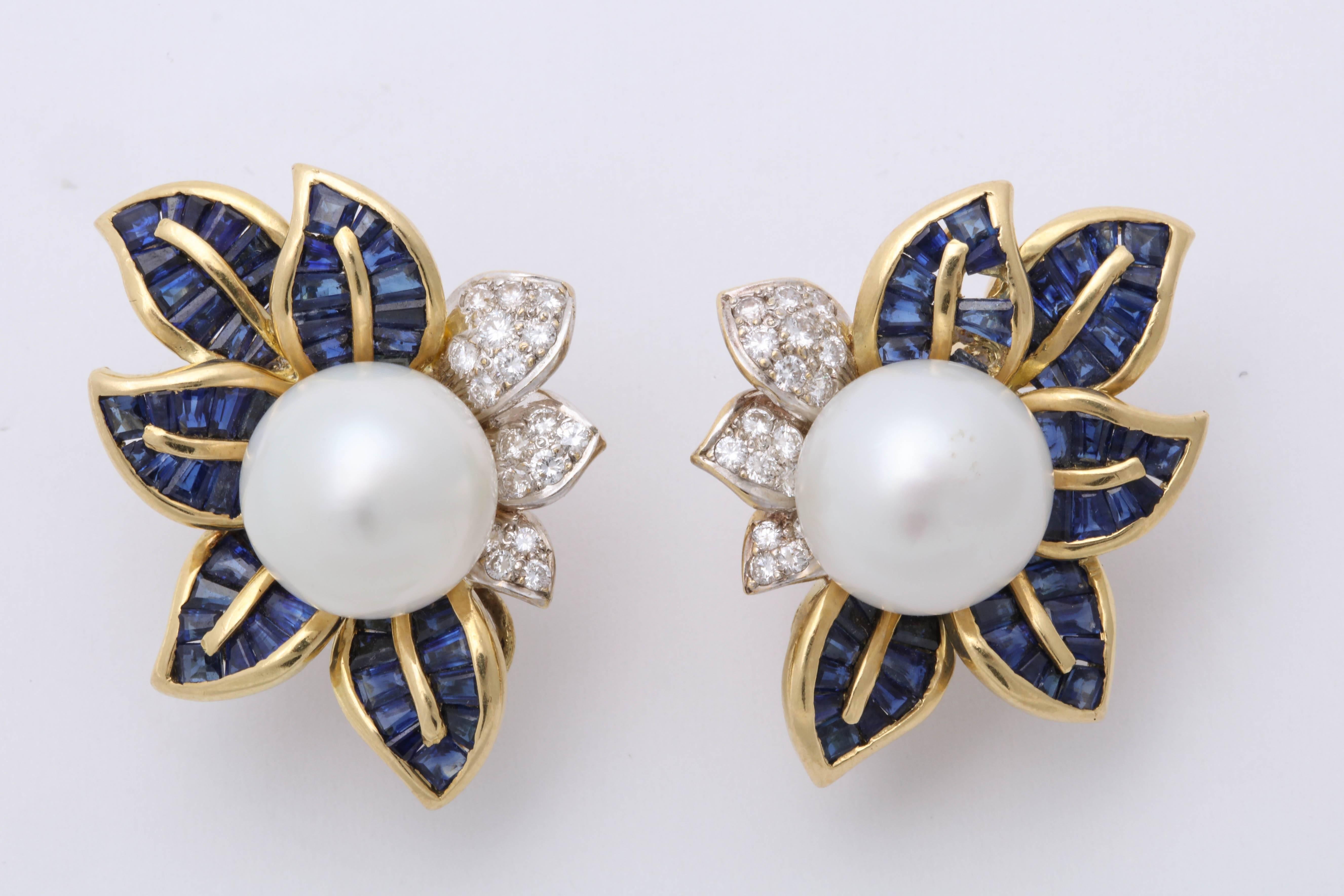 One Pair of Ladies Flower And Leaf Design earrings embellished With Two South Sea Pearls Measuring Approximately 14MM each. Each earring Is Further Decorated With Numerous Calibre Cut Custom Cut Sapphires Weighing Approximately 5 Carats Total