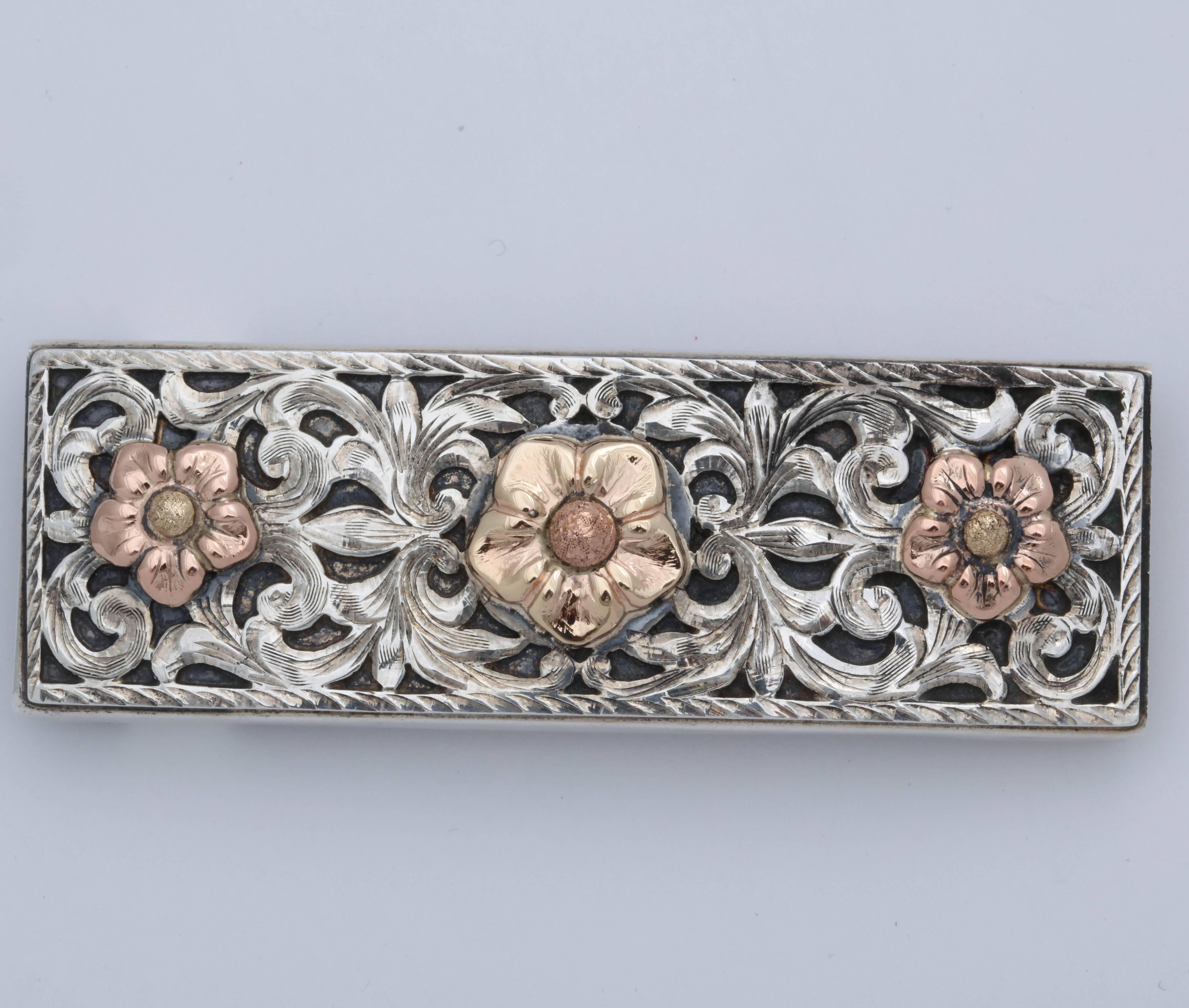 This beautiful belt buckle is hand engraved and hand made by Sun West . There are 2 layers of silver. The engraved first layer has 3 flowers applied in 14 kt rose gold and 14 kt yellow gold.  The second layer is oxidized  so that the engraved layer