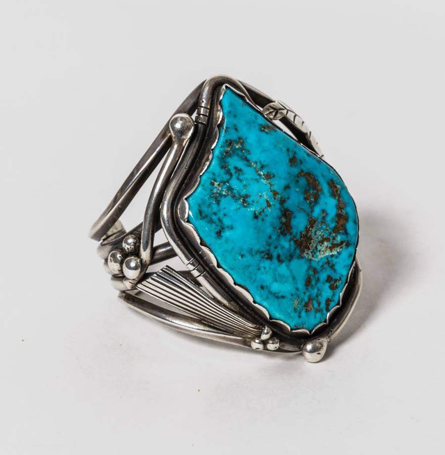 This is an exceptional  heavy American Indian silver cuff showcasing a stunning huge turquoise stone. This is an unsigned piece however we do believe it to be Navajo in origin. The silver work is beautifully done and features carved leaves and a