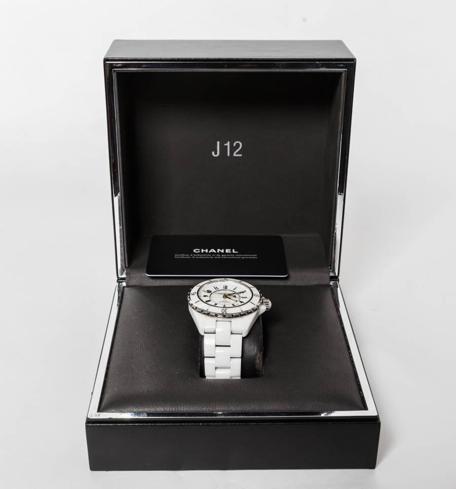 Ladies' stainless steel 39mm Chanel J12 automatic watch with rotating bezel, white flat dial, luminous, black numeral hour markers, calendar aperture between 4 and 5 o'clock, fluted push/pull crown, and white ceramic bracelet.

Comes with original