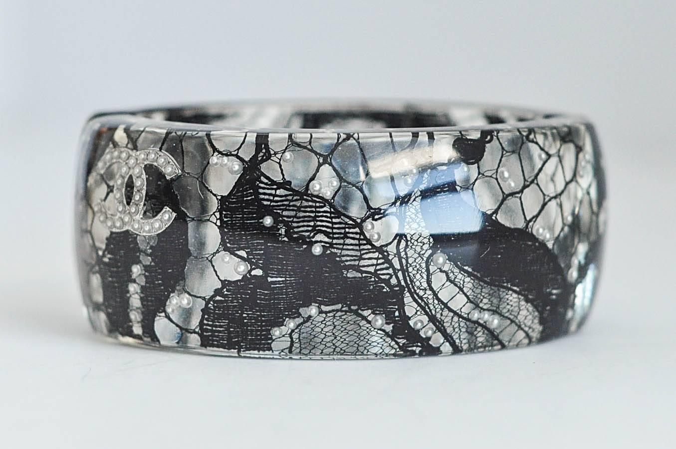 Exquisite oval, hinged cuff bracelet with magnetic closure by Chanel from 2013 collection.  Small pearls are scattered over a black lace fabric that is embedded in the lucite, creating both a modern and traditional design. In excellent condition.  