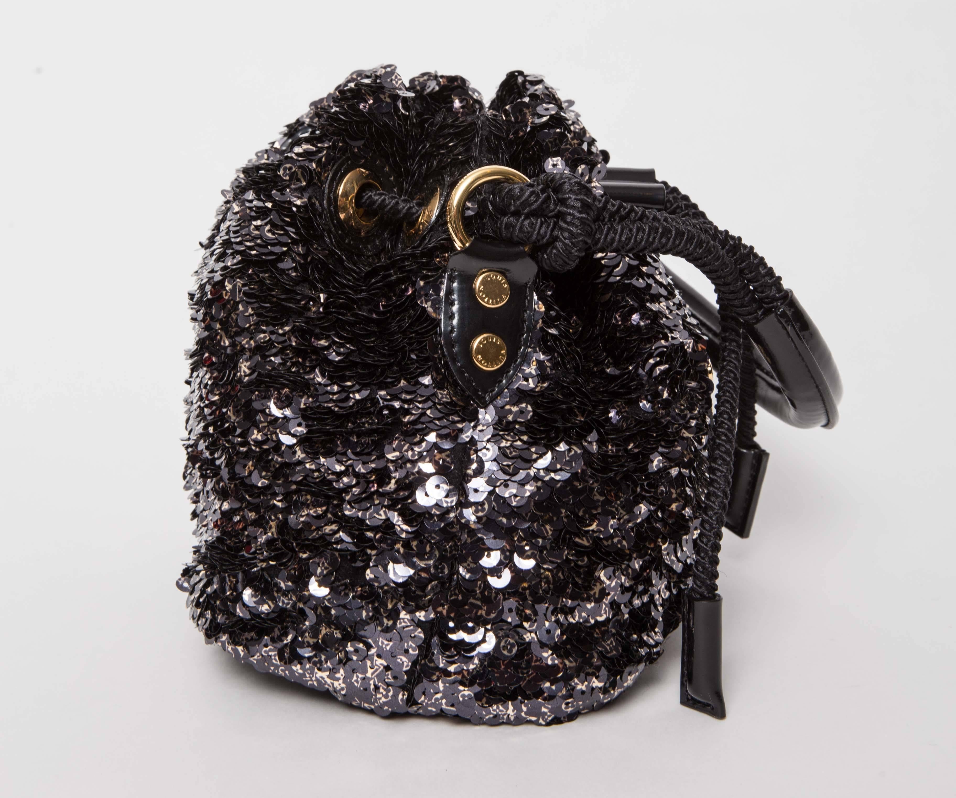 Louis Vuitton Limited Edition Black Mini Noe Rococo Bag features black logo sequins with black glossed patent leather and textile lining. Interior has one flat pocket and one lipstick pocket. Gold tone hardware and drawstring closure.
Handle drop