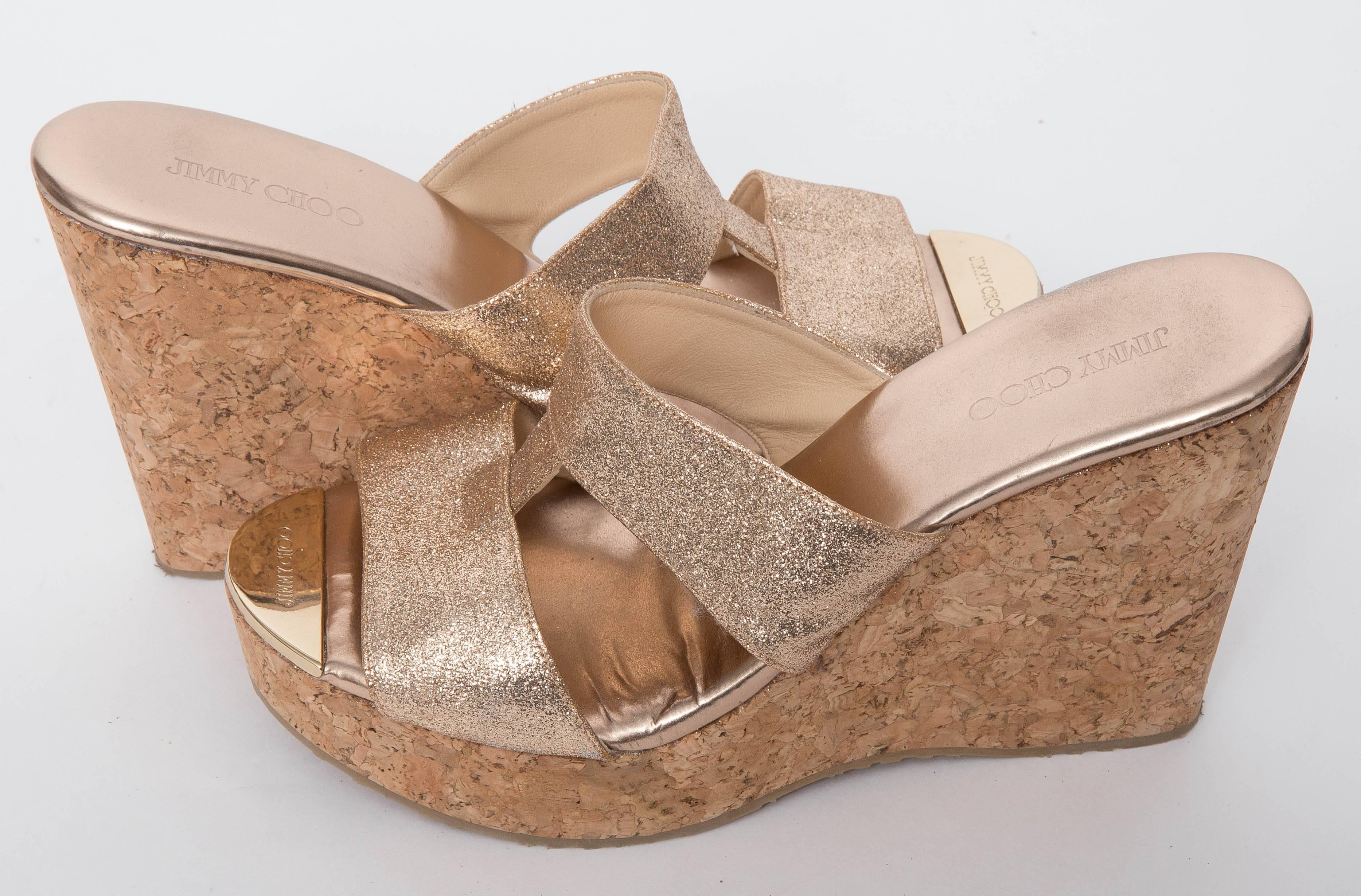 Jimmy Choo Porter Glitter Wedge Sandal in Gold features fine glitter and mirrored leather slide, tonal top-stitching,T-strap connecting double front bands, open-toe with golden logo-engraved plate, and added leather insole.
Does not come with