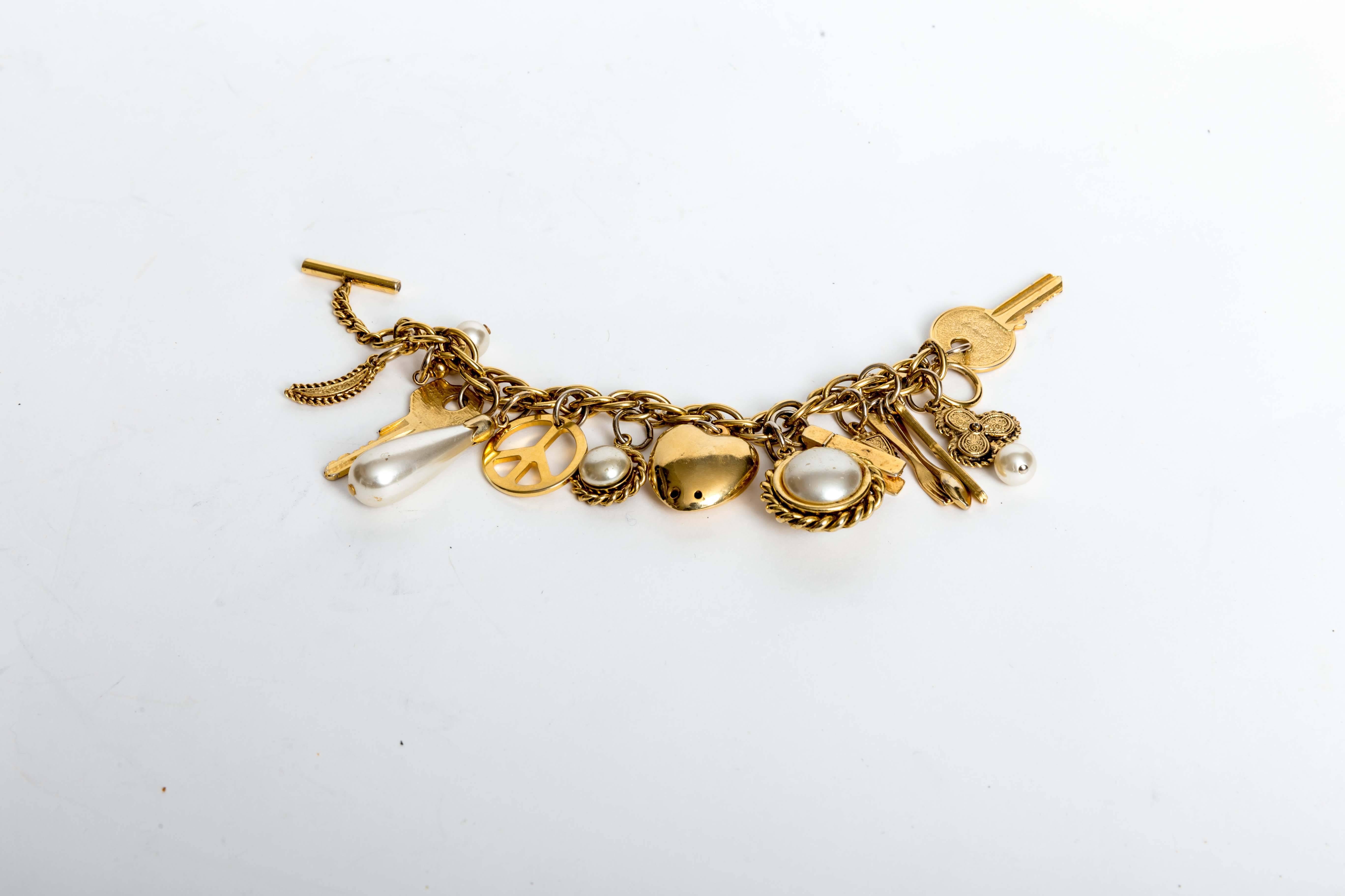 Signed Moschino Charm Bracelet with Pearls and Gold Charms. Charms include a puffed heart, key, three leaf clover with pearl drop, clothes pin and peace sign to name a few. There are a total of 14 charms with a toggle closure. This is a fun piece of