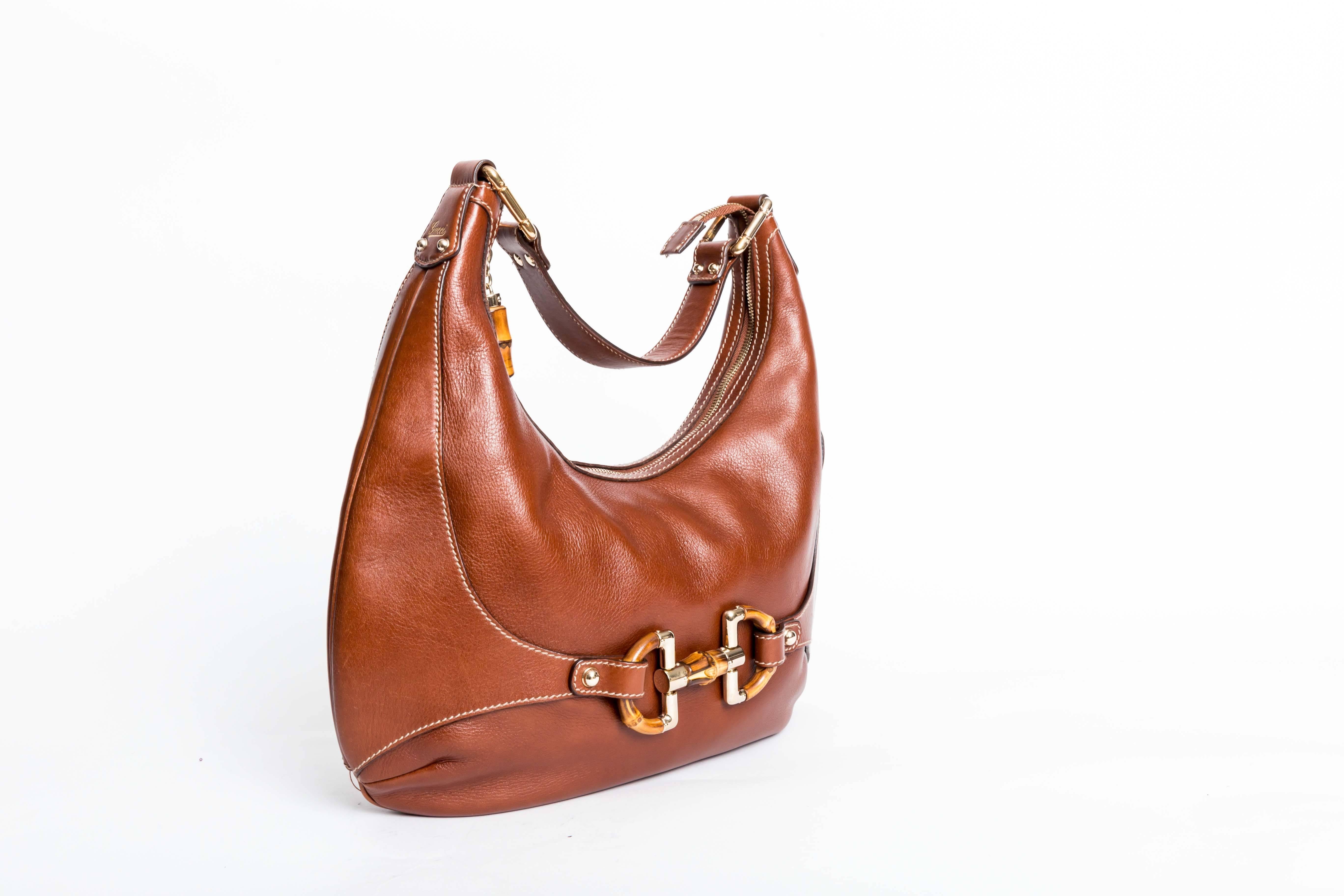 Gucci Horsebit Saddle Bag in Brown Leather. Bamboo iconic horsebit adorns the front of this beautiful bag. Zip Top with Bamboo Pull. Bag measures 14 inches in length and 9.5 inches at the center of the bag graduating to 15 inches at each end. The