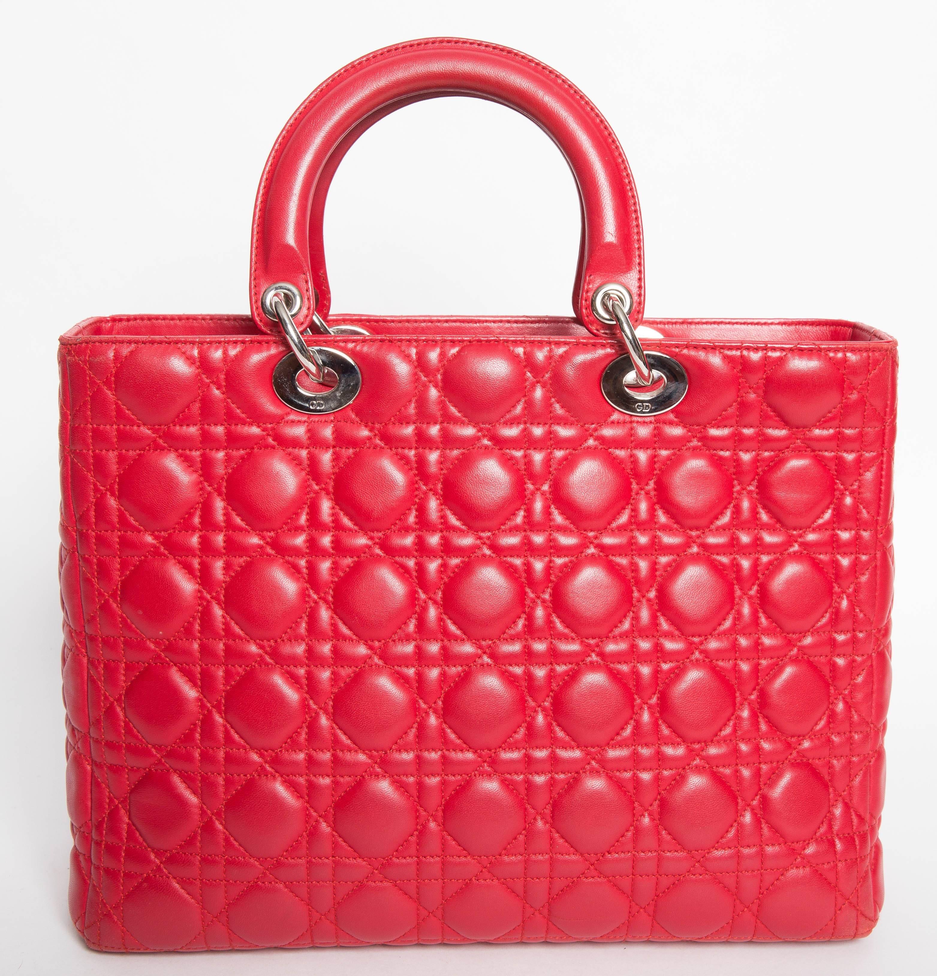 From the 2013 Collection. Red lambskin leather Christian Dior Large Lady Dior bag with silver-tone hardware, tonal stitching throughout, dual flat top handles, logo charm at front, red logo lining, single zip pocket at interior wall and zip closure