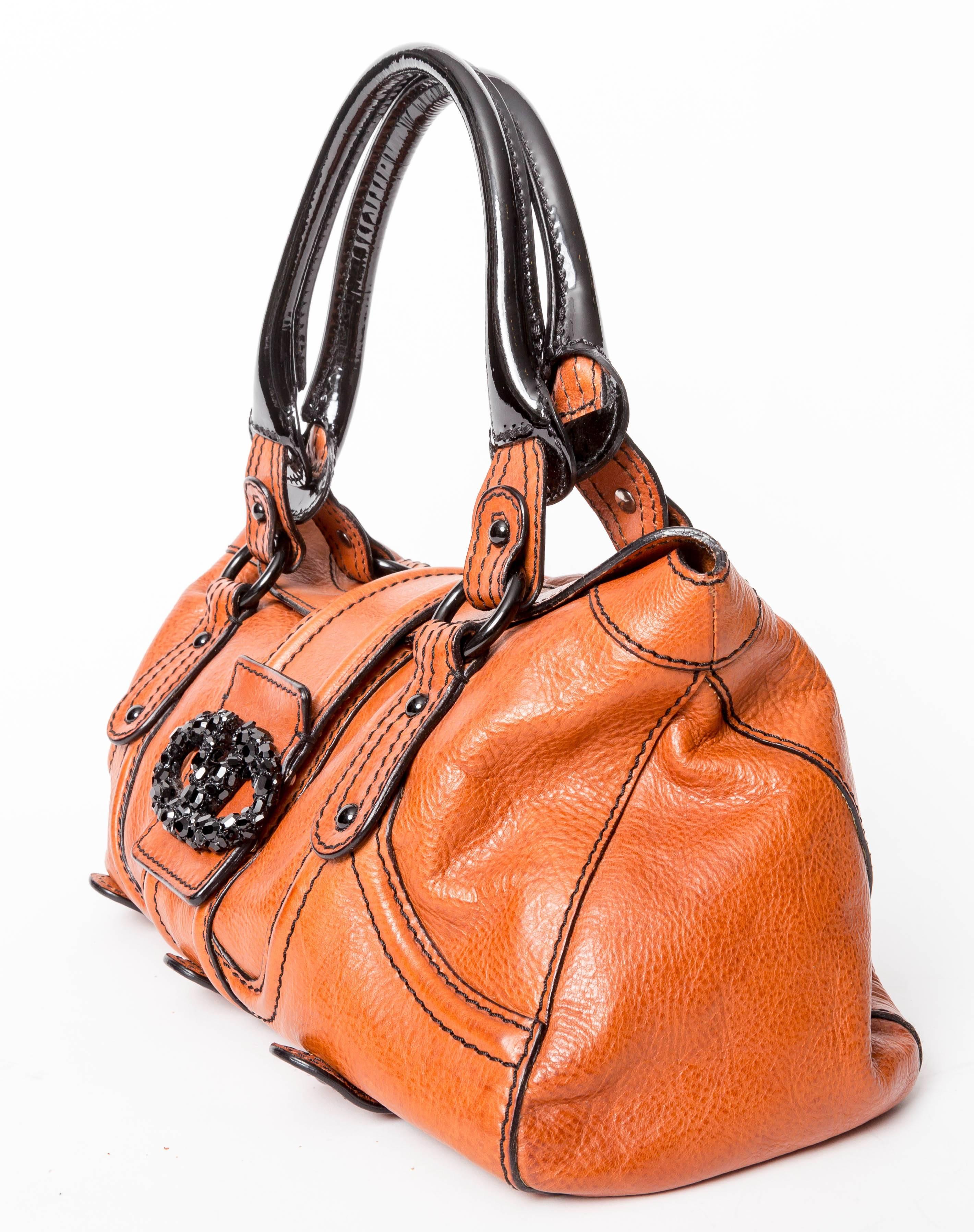 Very pretty Valentino bag in cognac leather with black patent straps and a gorgeous black swarovski crystal Valentino logo clasp. Bag closes with a strap across the top ending in one snap. This bag has one inside zip pocket and a black fabric
