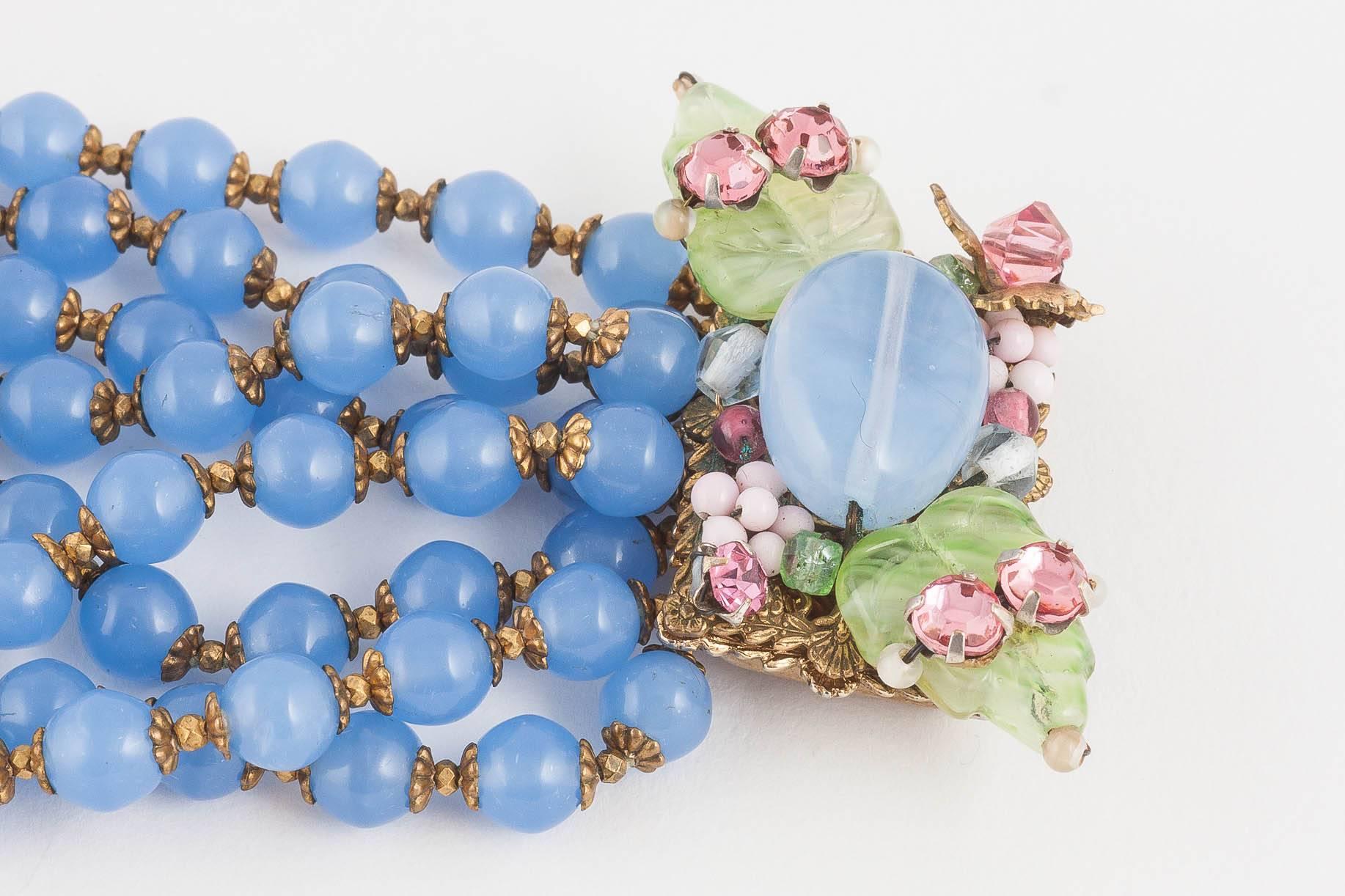 A charming and softly coloured hyacinth/chalcedony blue glass bead eight row bracelet, with moulded glass 'leaves' and assorted coloured pastes on the clasp, by Miriam Haskell , from the 1960s. With characteristic tiny hammered gilt spacers between