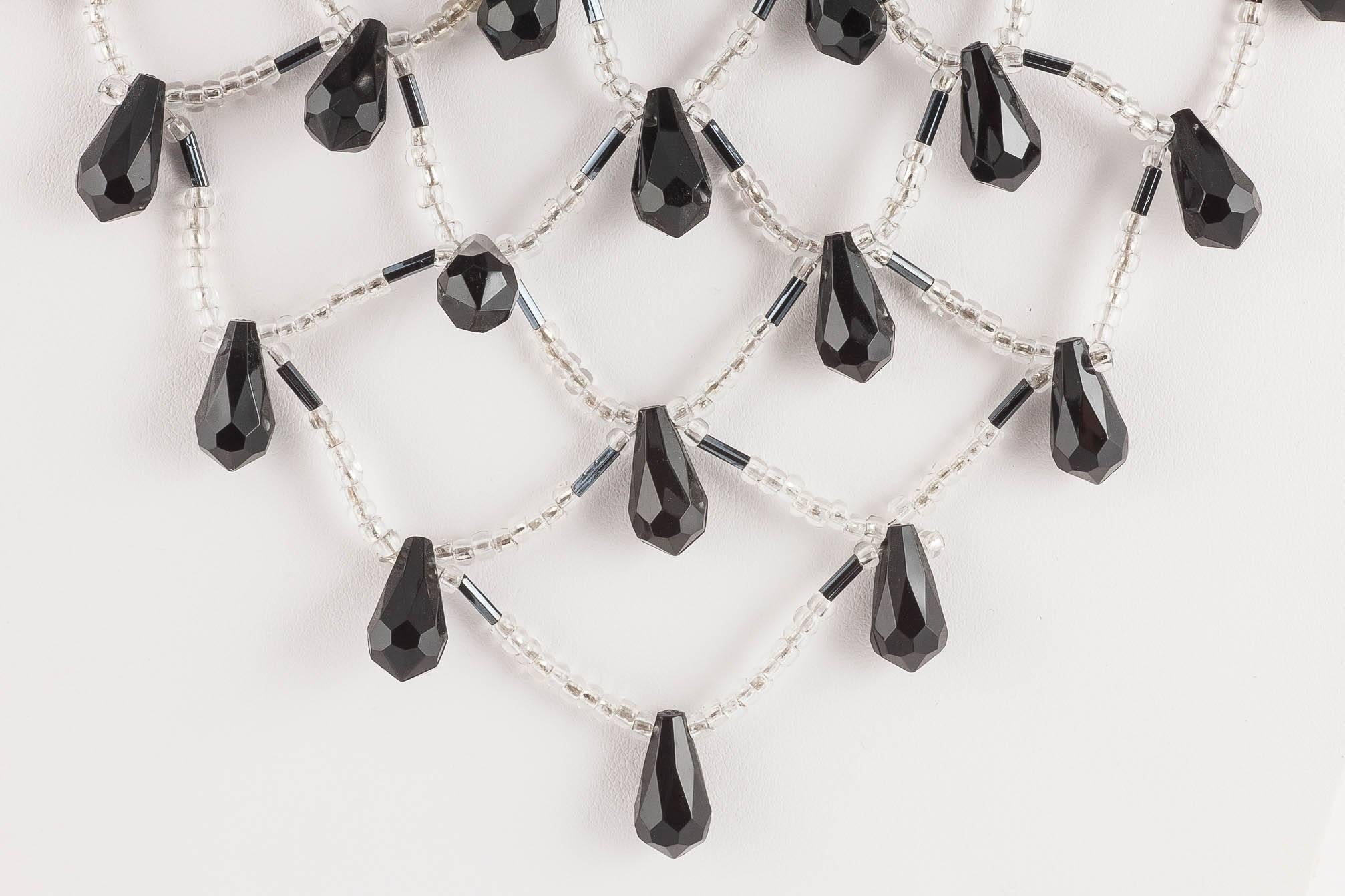 This striking bib necklace is made from larger plastic faceted teardrop beads, and haematite coloured bugle beads and clear round beads, all put together in an intricate woven design, looking dramatic and eye catching. Plastic beads were used as to