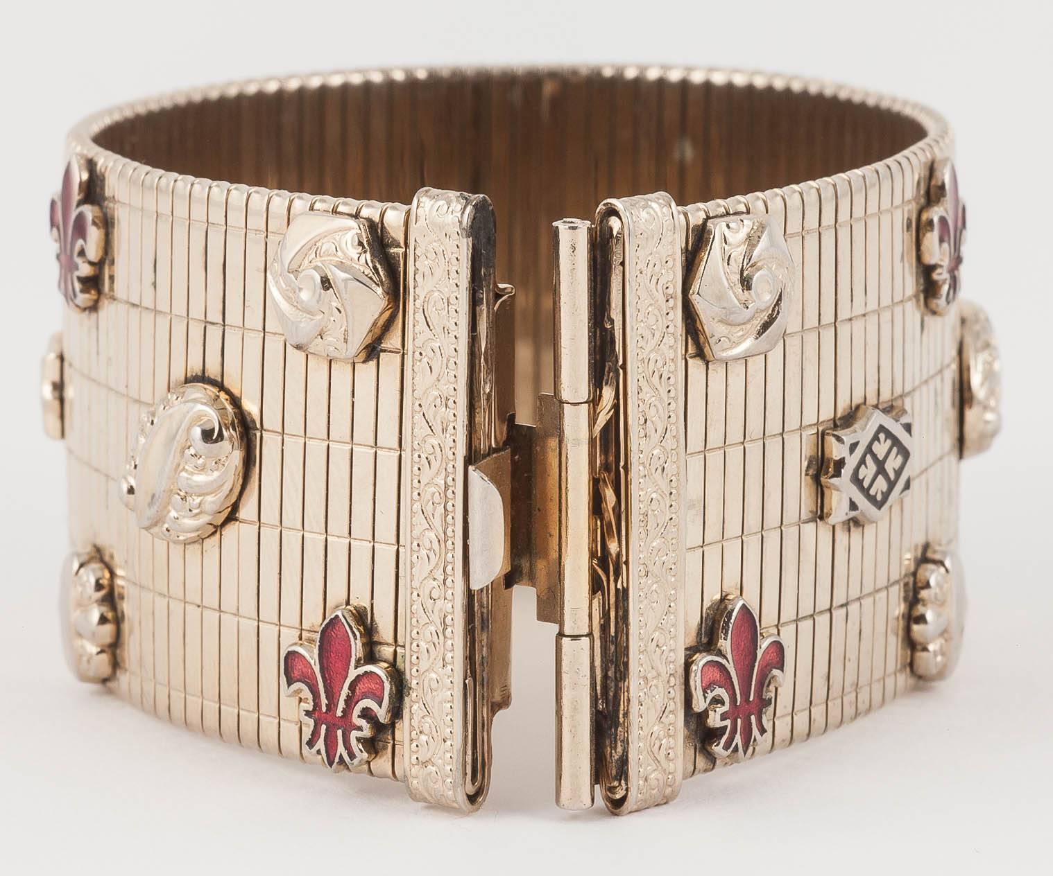 This is such a smart retro bracelet, featuring a cuff shape bracelet which moulds to the wrist like a huge watch strap and has enamelled 'fleur de lys' motifs and other small mounted plaques. The effect is very sophisticated 1940s tailored glamour.