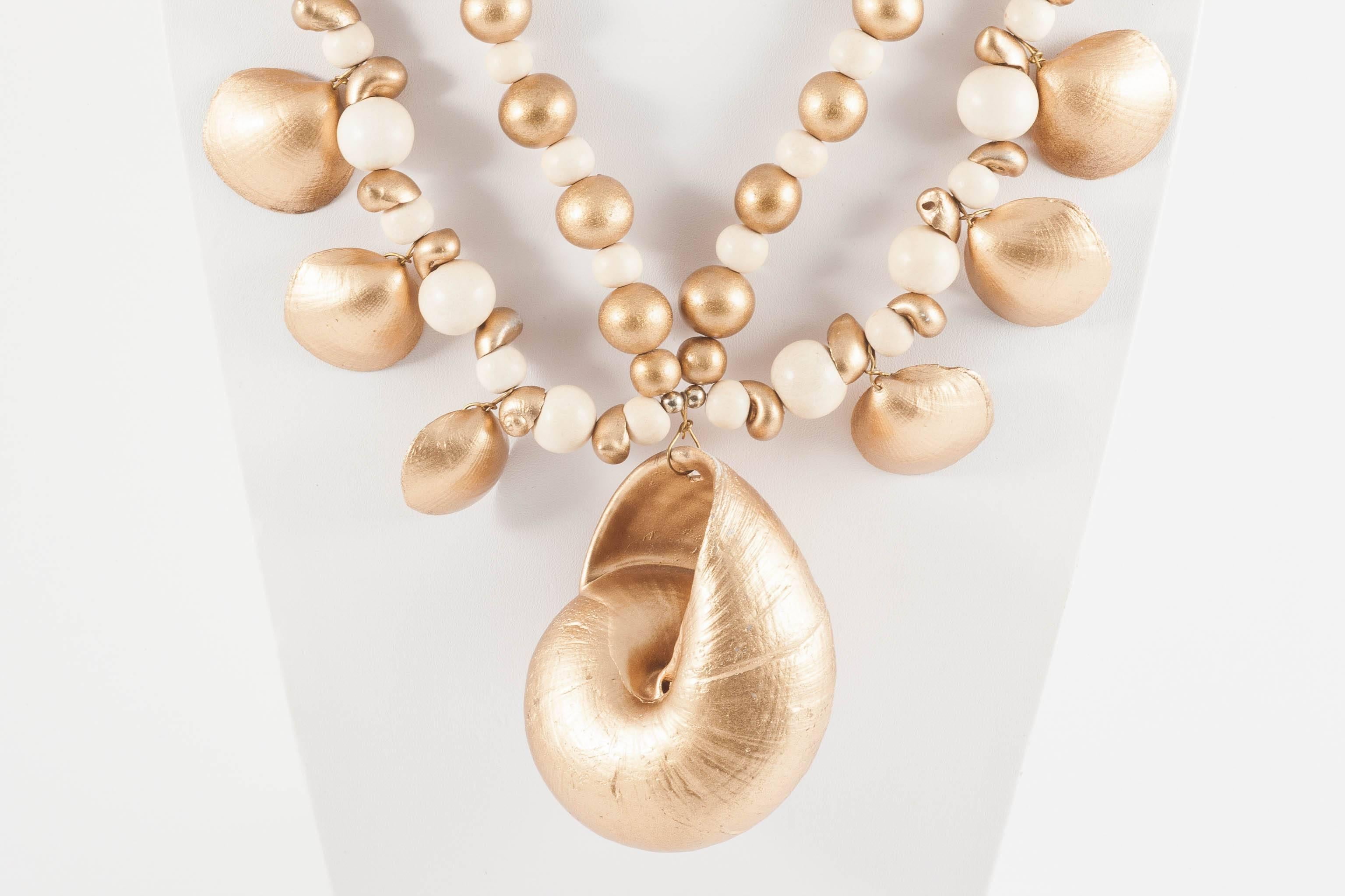 This very large, highly flamboyant and decorative necklace, with large central gilded shell pendant, made from cream and gilded wooden round beads, and gilded shells of assorted shapes and sizes, is fun, dynamic and exotic and  would be sensational