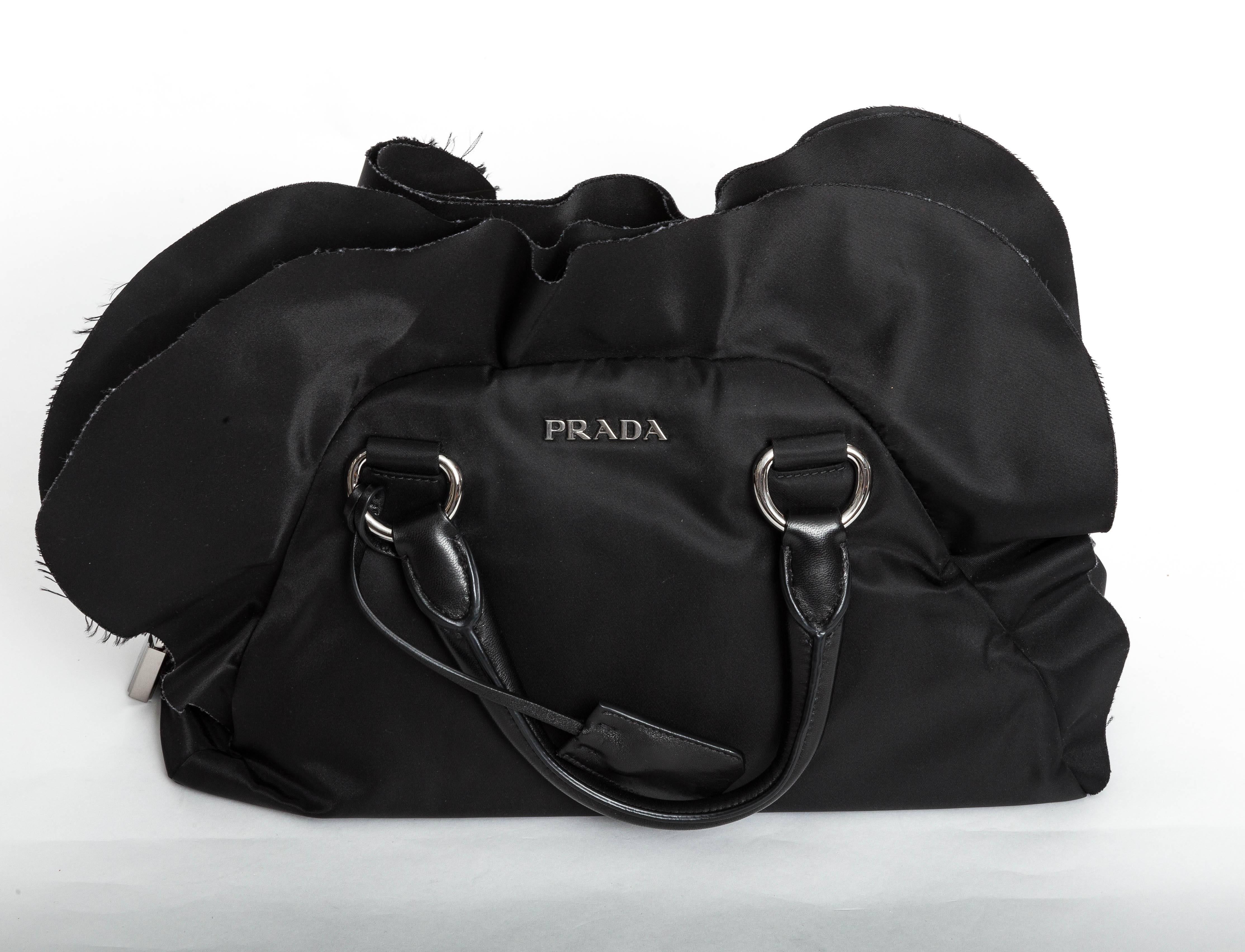 Prada Black Tessuto Nylon Ruffle Bauletto Bag
This wonderful Prada bag features Tessuto nylon with gorgeous pleated ruffled detail at the top of the bag and a large silver Prada padlock on one side.
Leather Handles contrast beautifully with the