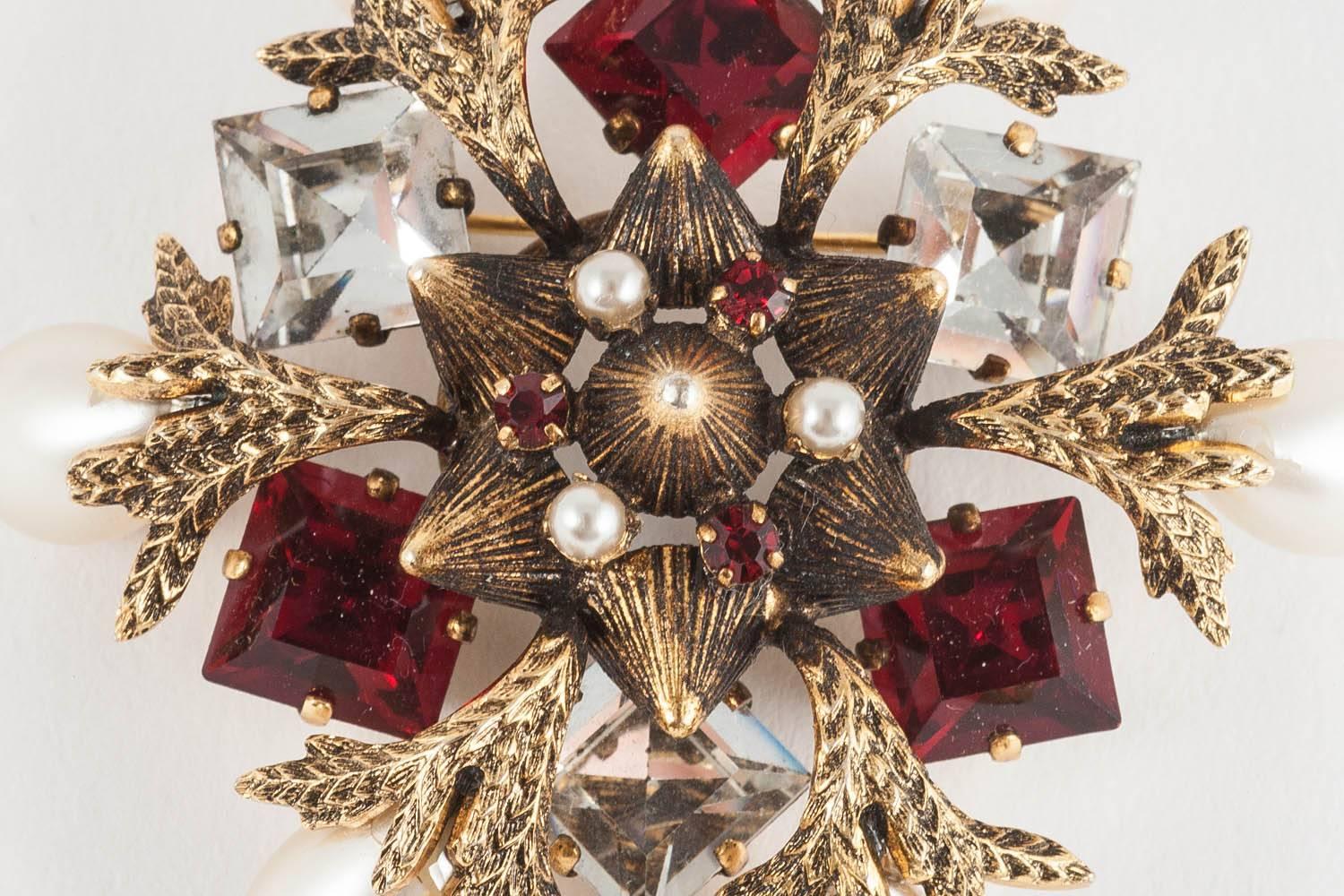 A charming subject translated into jewel form, this brooch is made from a textured gilt metal, formed into points in the centre of the brooch and forming 'branches' holding the teardrop shaped pearls. Set with square cut ruby and clear pastes