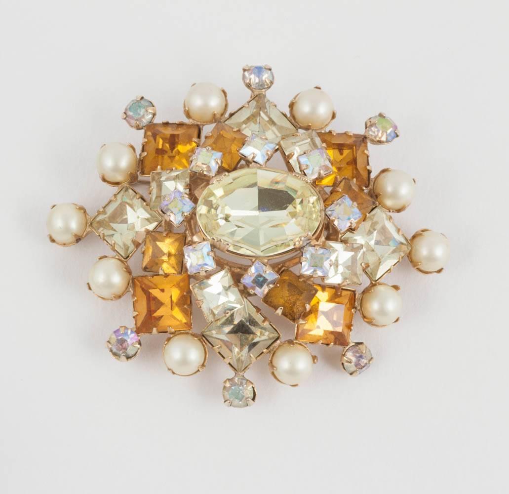 A jewelled gem brooch, in gilt metal, set with citrine and topaz paste square and oval  stones, with iridescent round paste highlights, and edged in paste pearls. It is very typical of this manufacture, a modest but striking brooch, very wearable, 