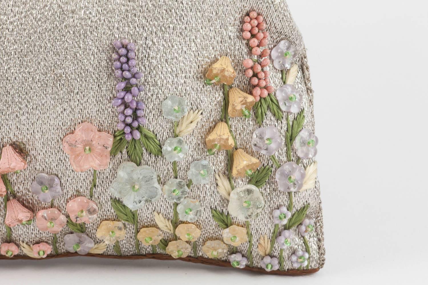 A charming little clutch bag, made from silvered fabric, attached by some fine webbing to a silver plated engraved frame. the silvered material is decorated with moulded glass flowers in muted pink, blue and citrine, hand painted from behind, and