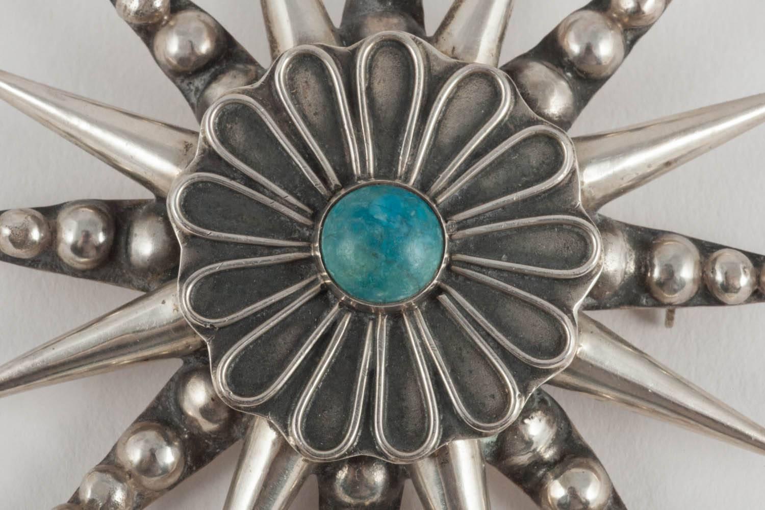 This is a dramatic Bohemian style pendant or brooch hallmarked, but not signed, with a makers mark. The two layers of pattern, on closer inspection, look like a star on the outside, and a daisy on the inner ring, with the lovely blue turquoise