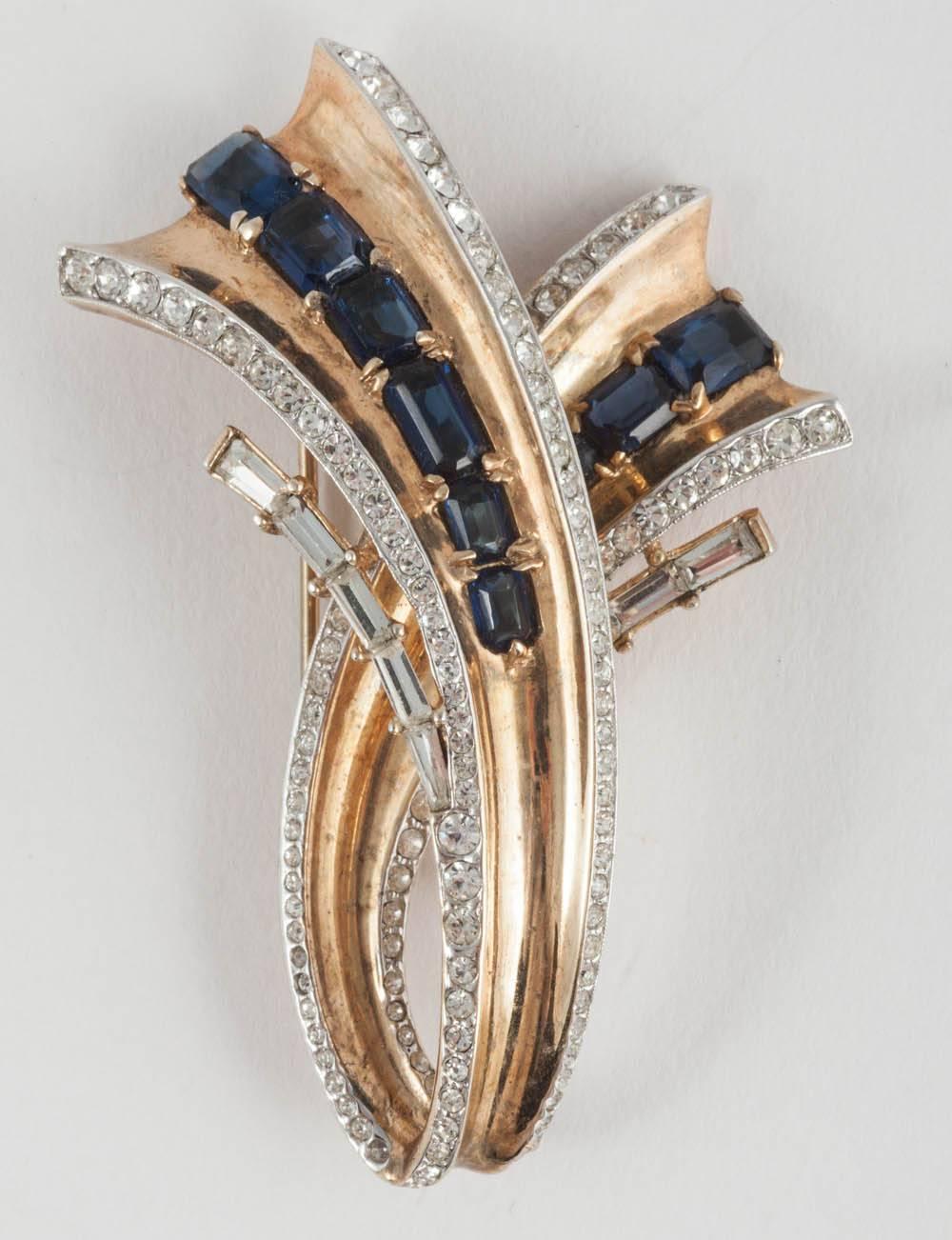 A strong and striking design by Alfred Philippe for Trifari, a highly stylised brooch and earrings, made from silver gilt, and set with clear and sapphire pastes, in varied cuts. The brooch has a 'fur clip' fitting ie. a double pronged clip/pin