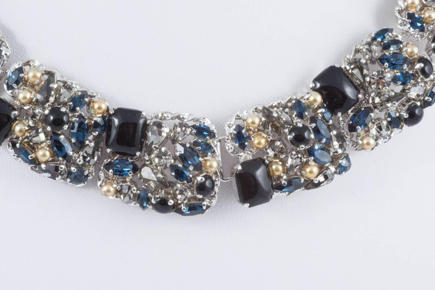 A rich melange of black cabuchon cushion cut paste, sapphire paste in assorted shapes, smokey grey paste, and paste pearls, all set in silvered metal, this parure, necklace and earrings, is dated 1963 and was made by Henkel and Grosse for Christian