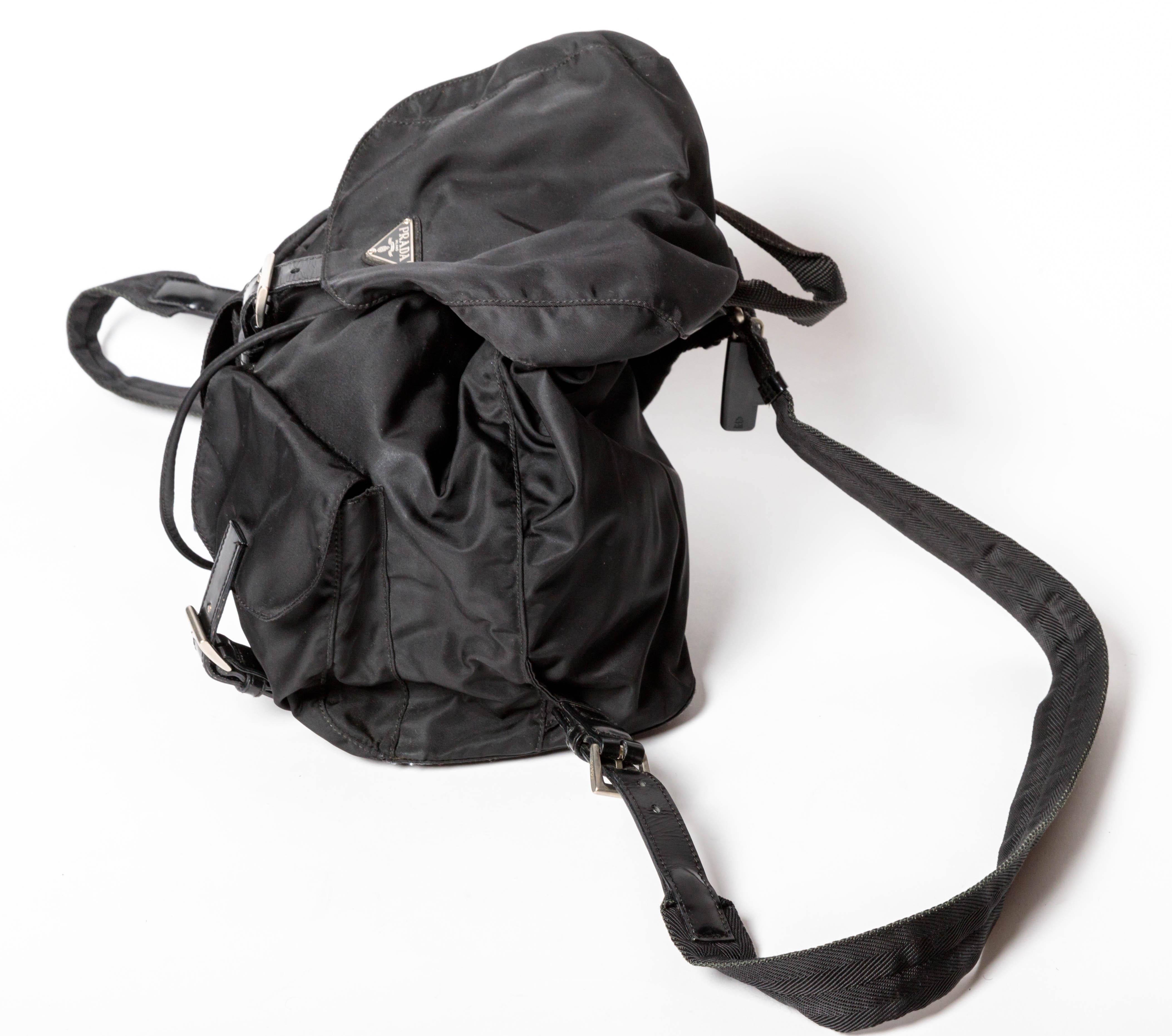 This is the perfect Prada backpack. 
Nylon with two front buckle pockets, this backpack can be opened using the toggle closure. A snap and buckle secure the main part of the backpack which has one interior zip pocket. in place. Canvas straps and top