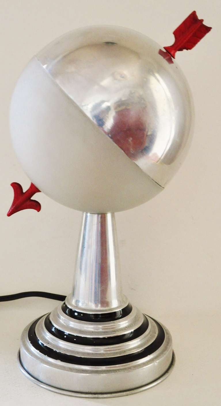 This pair of American Art Deco aluminium armillary styled accent table lamps feature hemispherical shades in frosted glass that are each pierced with a red enameled arrow. The stepped base features bands of black enamel. They are both in excellent