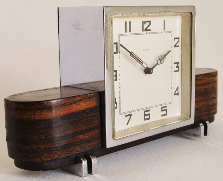 This very elegant chrome plated desk clock with Macassar veneered 'wings' has  wonderful Art Deco features from its overall design to its classic feet and hands. It is finished both front and back and as such it is a true desk clock. Its condition