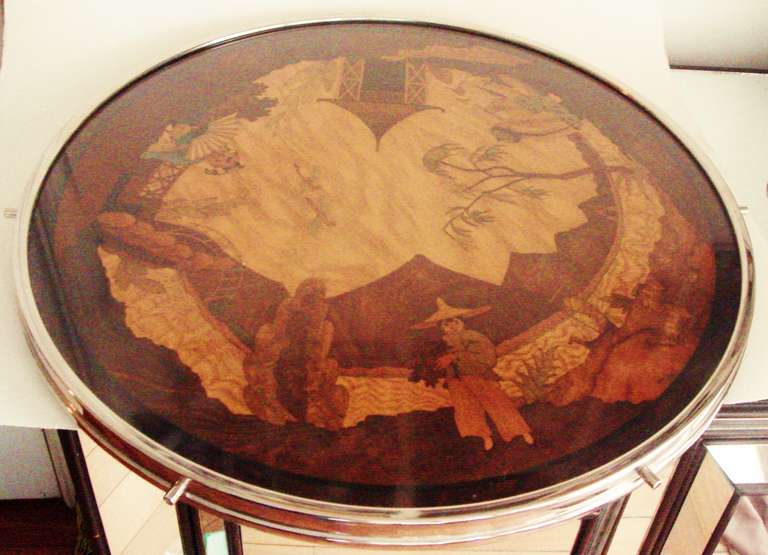 The surface of this very large German Art Deco Lazy Susan is a glass covered painted wood panel that is decorated with classic chinoiserie scenes. This rests on a wooden top that is banded by a frame of nickel plated brass, impressed with the WMF