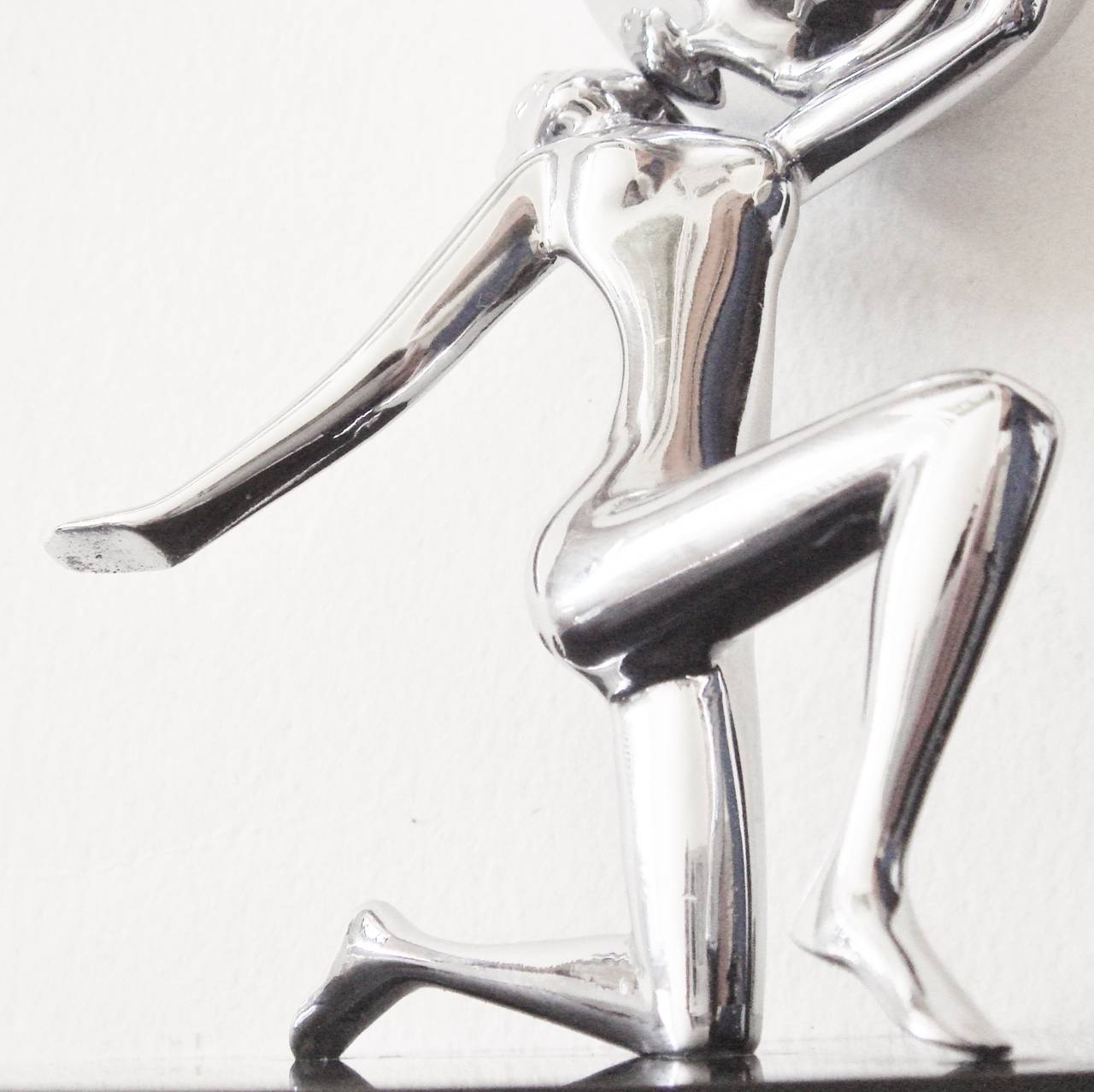 This English Art Deco chrome plated stylized nude holds a ball containing a wheel and flint lighter and kneels on a square of black Perspex/Lucite. The nude is clearly fashioned after the Hagenauer figures of the period  and, while  not of the same