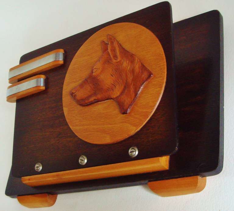 The ultra Art Deco look of this wall mounted magazine or letter rack was obviously designed with the dog lover in mind. It features a wooden etched German Shepherd head cut out and in relief on a blonde wood disc.This is mounted to the body of the