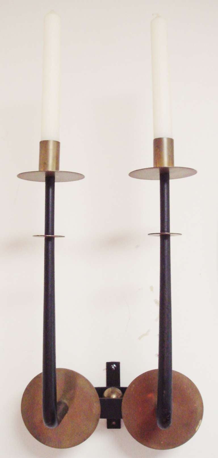 This very elegant pair of American Mid-Century Modern wall mounted twin candle sconces are in the style of Tommi Parzinger. They are extremely well constructed with twin shafts in hand-hammered forged iron that are finished in matte black. Each
