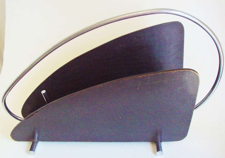 This Australian Mid-Century chrome and black stained wood, floor standing magazine rack has a wonderful biomorphic shape to the wood sides and is accented with a chrome whiplash carrying handle with a pair of chromed steel tubular feet. Both the