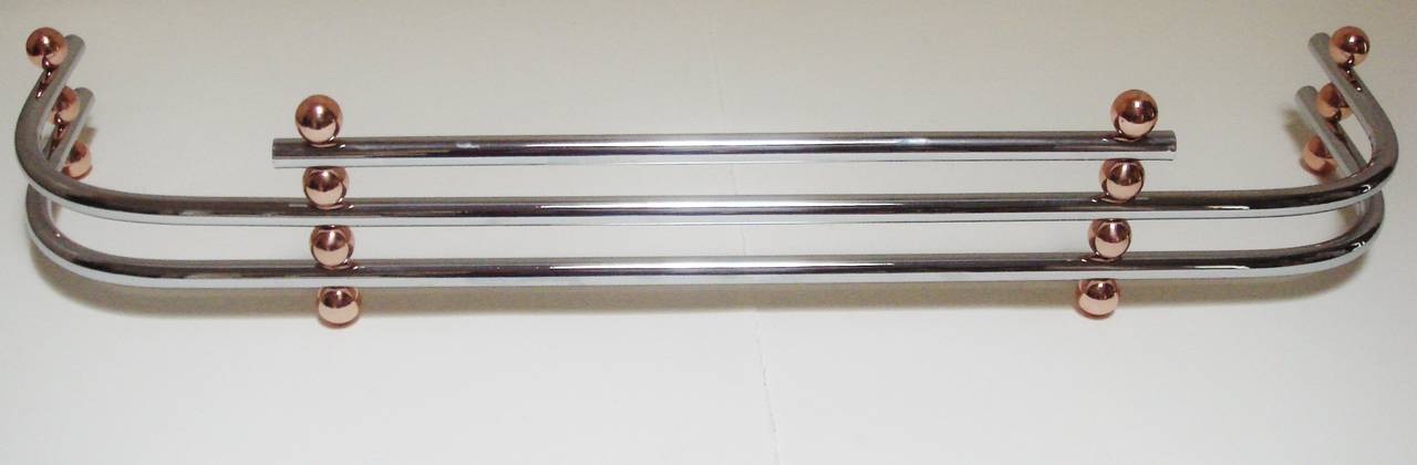 This American Art Deco chrome and copper andirons and fender set has been totally restored to fabulous effect. It features the more elaborate and seldom seen three tubular bar chrome fender accented with no less than fourteen 1