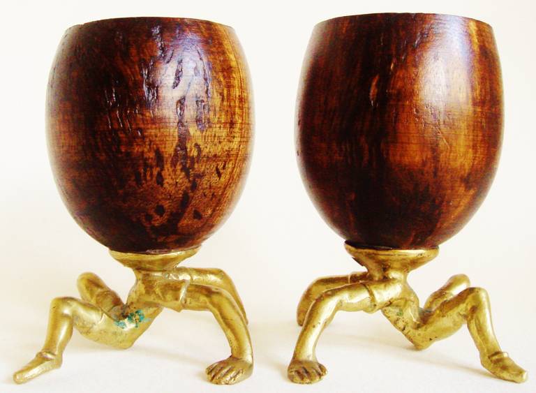 This is a rare bizarre pair of real coconut shell cups that replace the heads of seated male gymnasts each dressed in t-shirt and shorts and resting back on their hands in the 