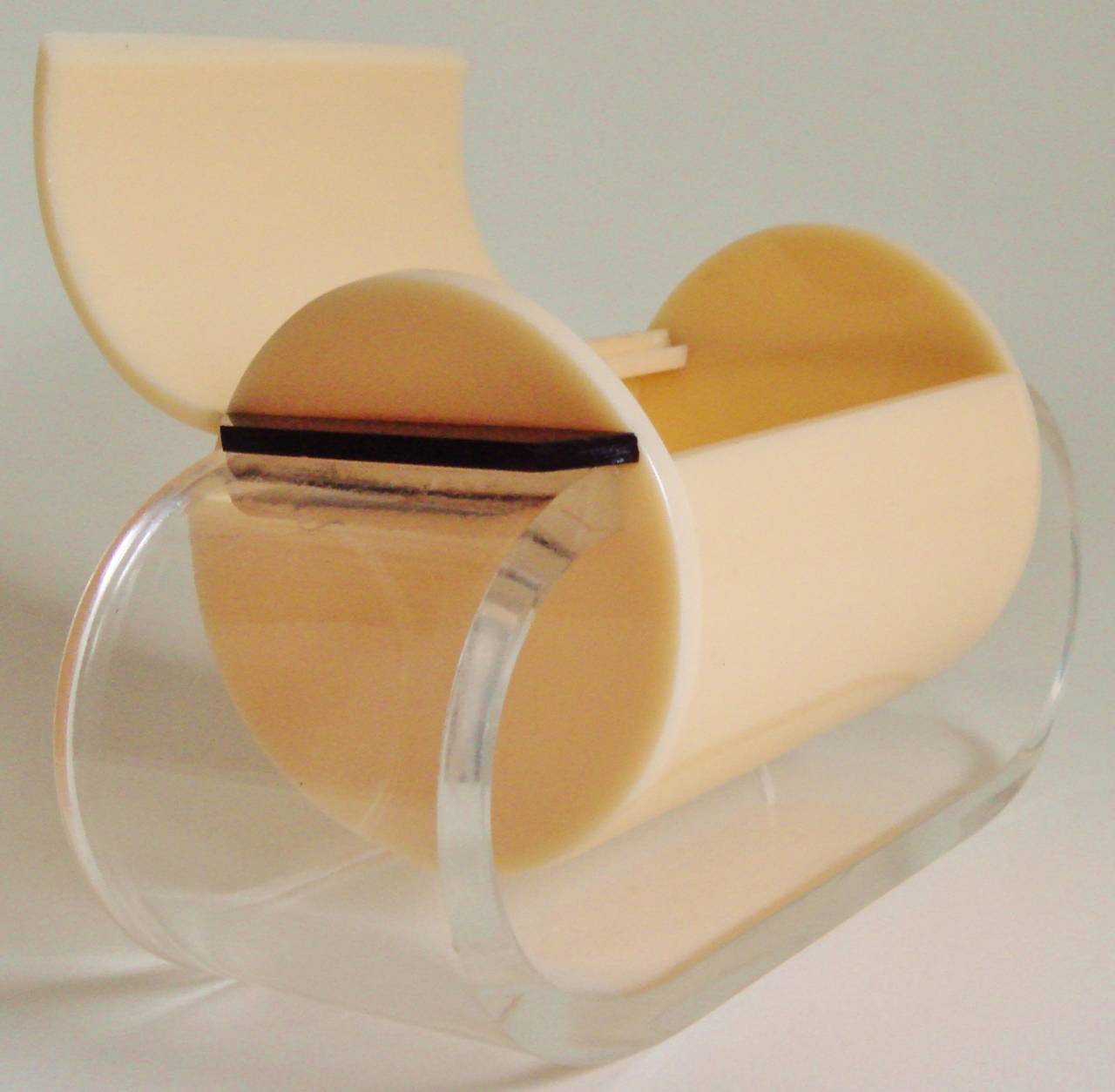 This rare and stunningly designed English Art Deco vanity box consists of a horizontal tubular barrel in peach Lucite with hinged lid and clear Lucite geometric handle. It is supported on a thick 