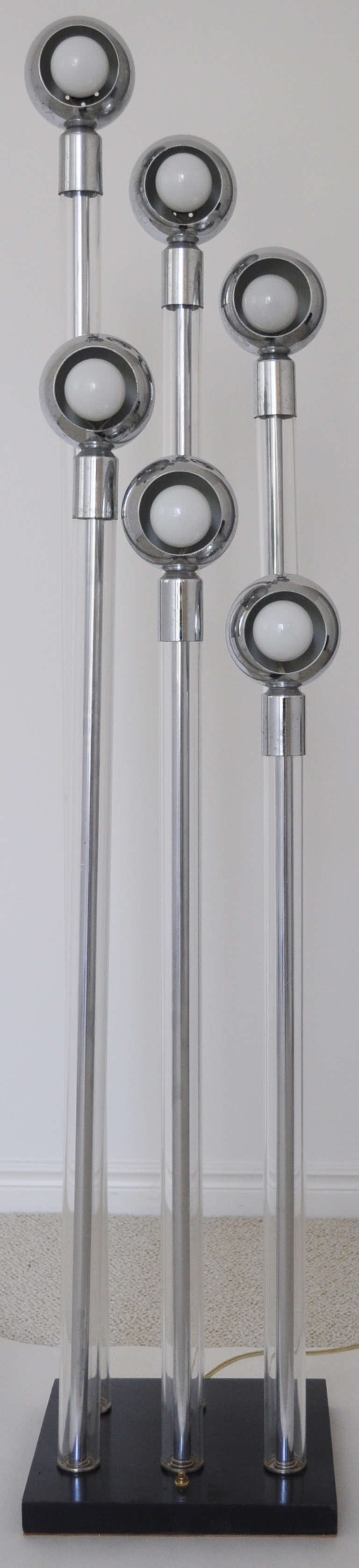 This American 1960s modern architectural fixture is composed of six eyeball lamps mounted on six graduated chrome rods surrounded by clear Lucite tubes. Each in turn is capped at the top by a chrome collar and at the bottom fixed to a thick black