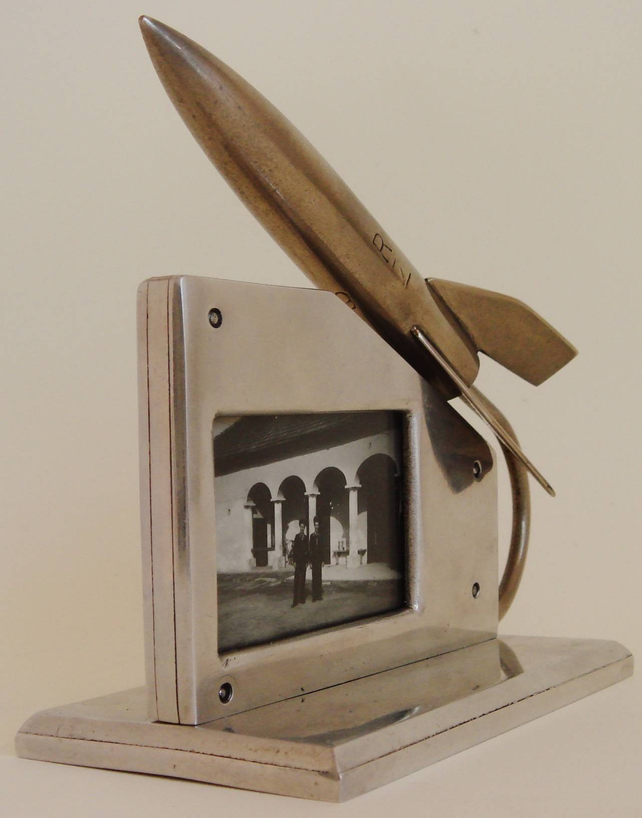This fabulous American, Jet-Age, Trench or Outsider Art polished aluminium and steel frame features an asymmetrical design with a polished steel rocket swooping up over it. The frame is double-sided and can be opened up to change the photographs by