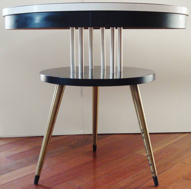 This American Mid-Century Modern two-tier occasional table features a top of bright matte white Arborite veneer (A material first invented in 1948) contrasted with a rim and second shelf in black lacquered wood. The whole is accented with brushed