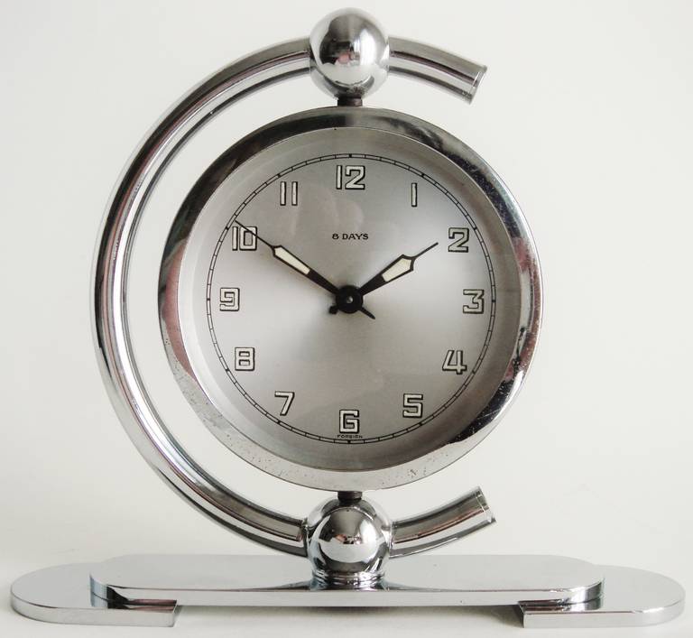 This very graphically designed German Art Deco chrome-plated, 8 day mechanical shelf clock features a swivelling face and movement housed in a strong geometric demi-lune bracket, decorated with spheres. The face displays the word 