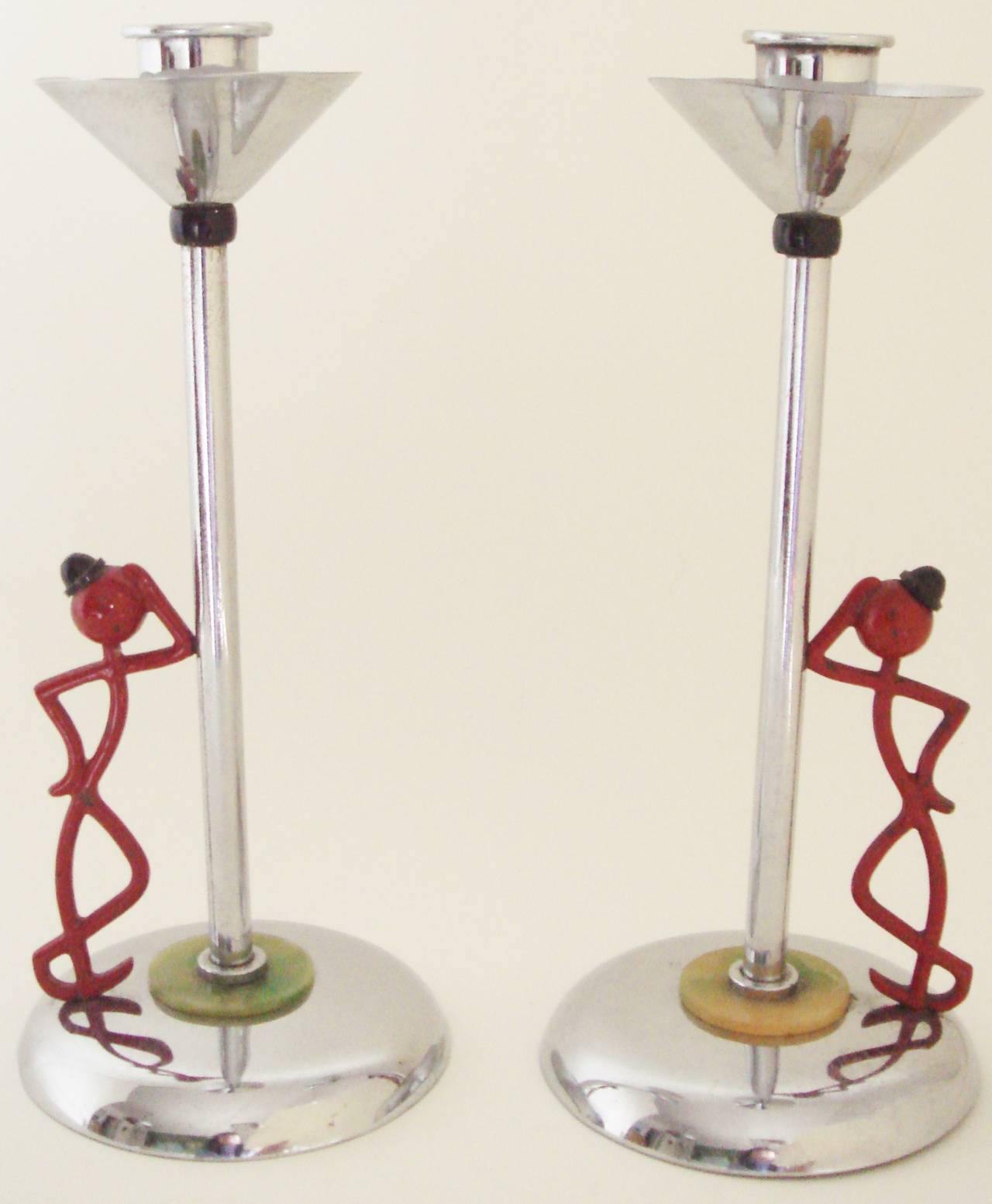 This fun and rare pair of English Art Deco chrome plated candlesticks are accented with green marbled Bakelite discs at the base and feature a cheeky red enamelled stick figure (the design of which is attributed to Hagenauer for GEC) sporting a