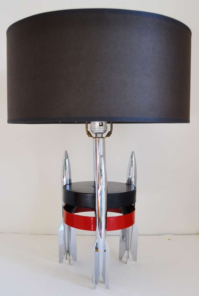 This great Art Deco Machine Age lamp features a central chrome column surrounded with a black lacquered wooden disc above a red lacquered metal band and all supported on three chrome-plated rocket 