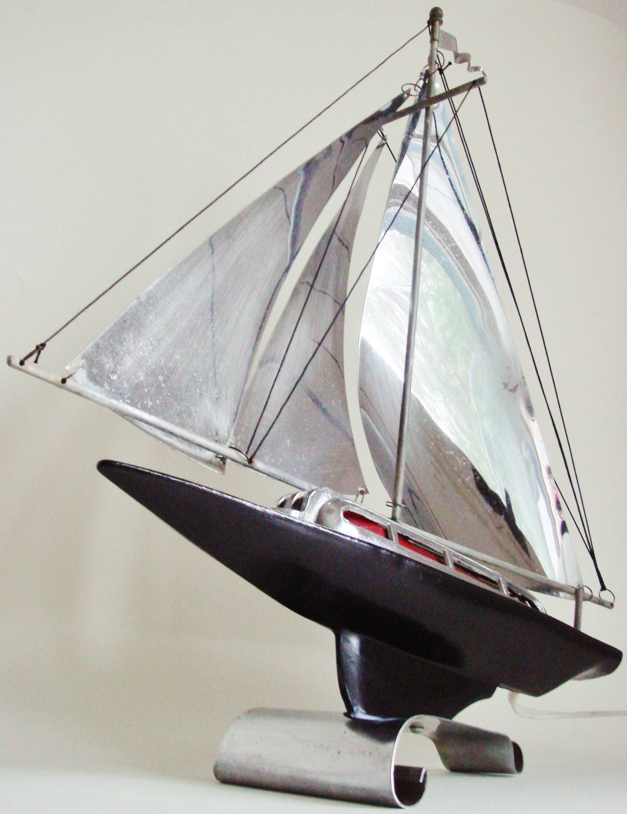 Questa lampada da tavolo americana Art Deco cromata e smaltata di nero ha la forma di uno yacht da corsa stilizzato e aerodinamico dell'epoca. Presenta una luce di cabina rossa sfumata che viene esaltata dalle vele cromate e illuminata tramite