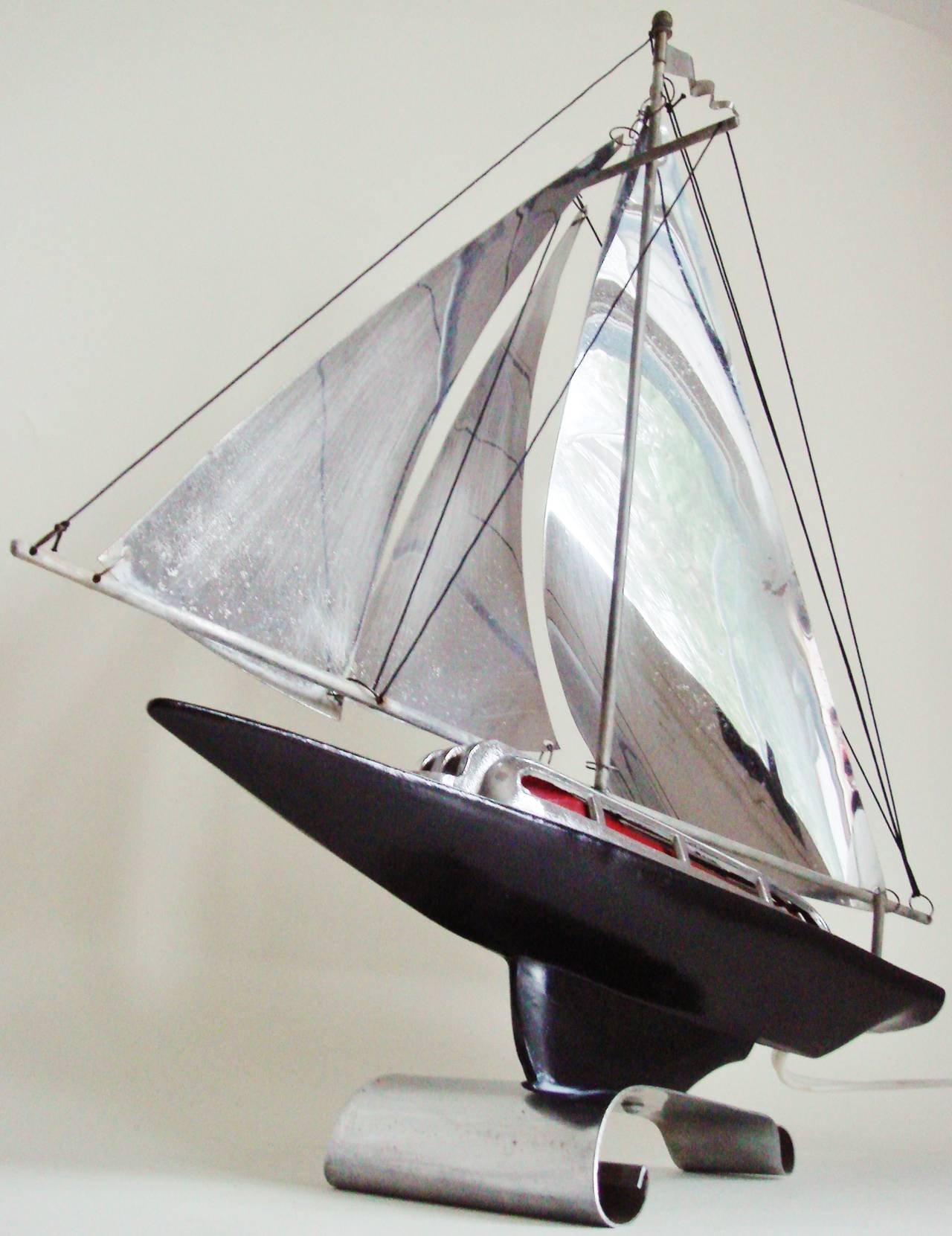 This American Art Deco chrome and black enamelled table lamp is in the form of a stylized streamlined racing yacht of the period. It features a red shaded cabin light that is enhanced by the chrome sails and illuminated by means of the original