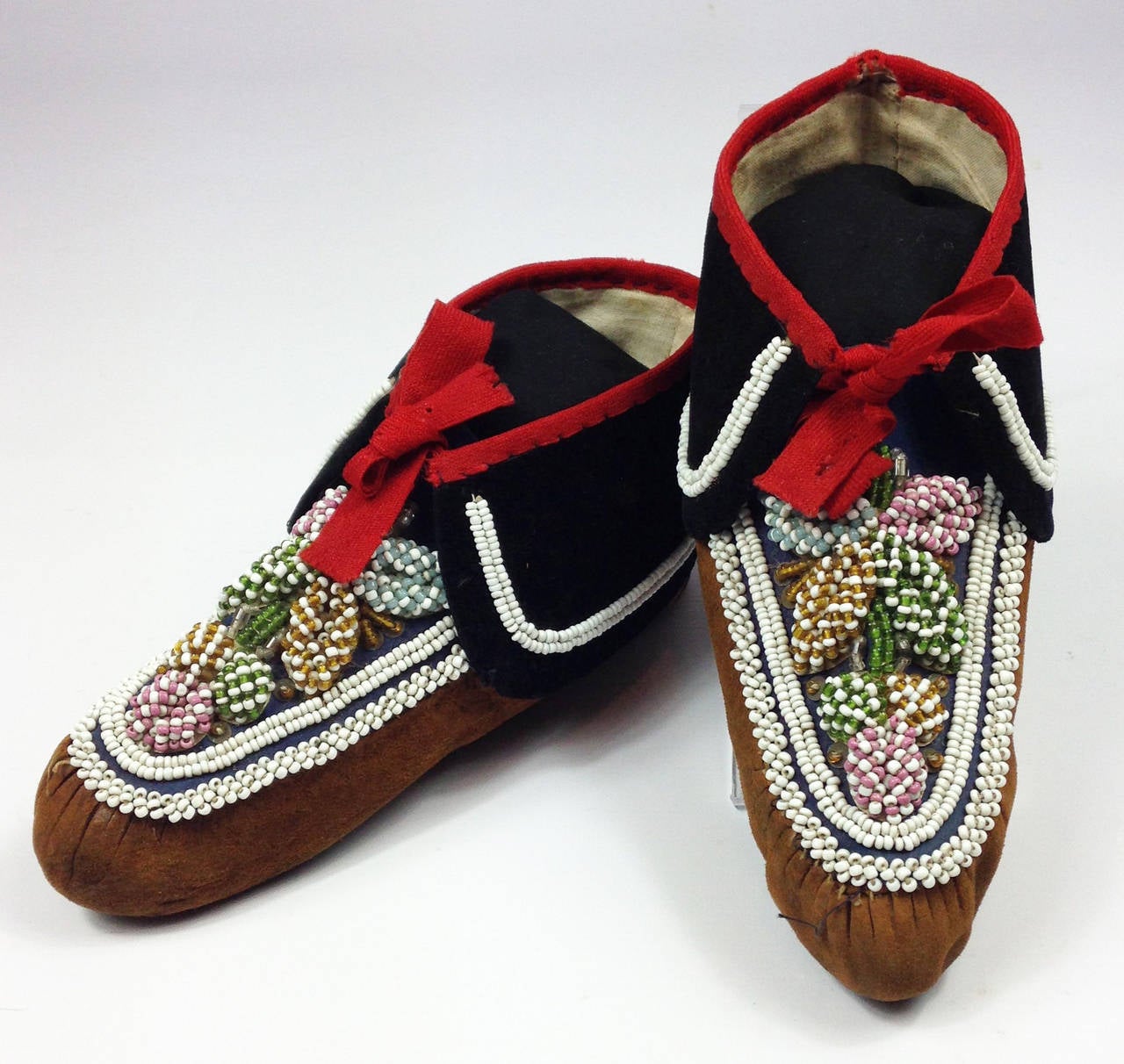A rare pair of Eastern Woodlands beaded hide moccasins.

Most probably Iroquois. Puckered toes, the vamps overlaid with a blue cotton which are decorated elaborately with floral designs and borders using several shades of opaque and translucent