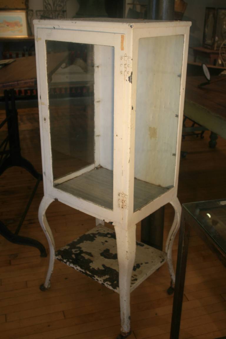 Early Doctor's cabinet, circa 1900. Wooden wheels and original white paint and beautifully made of cast steel. Could be stripped to natural steel. All original glass on three sides. Great cabriole legs. Classic design is sculptural as well as