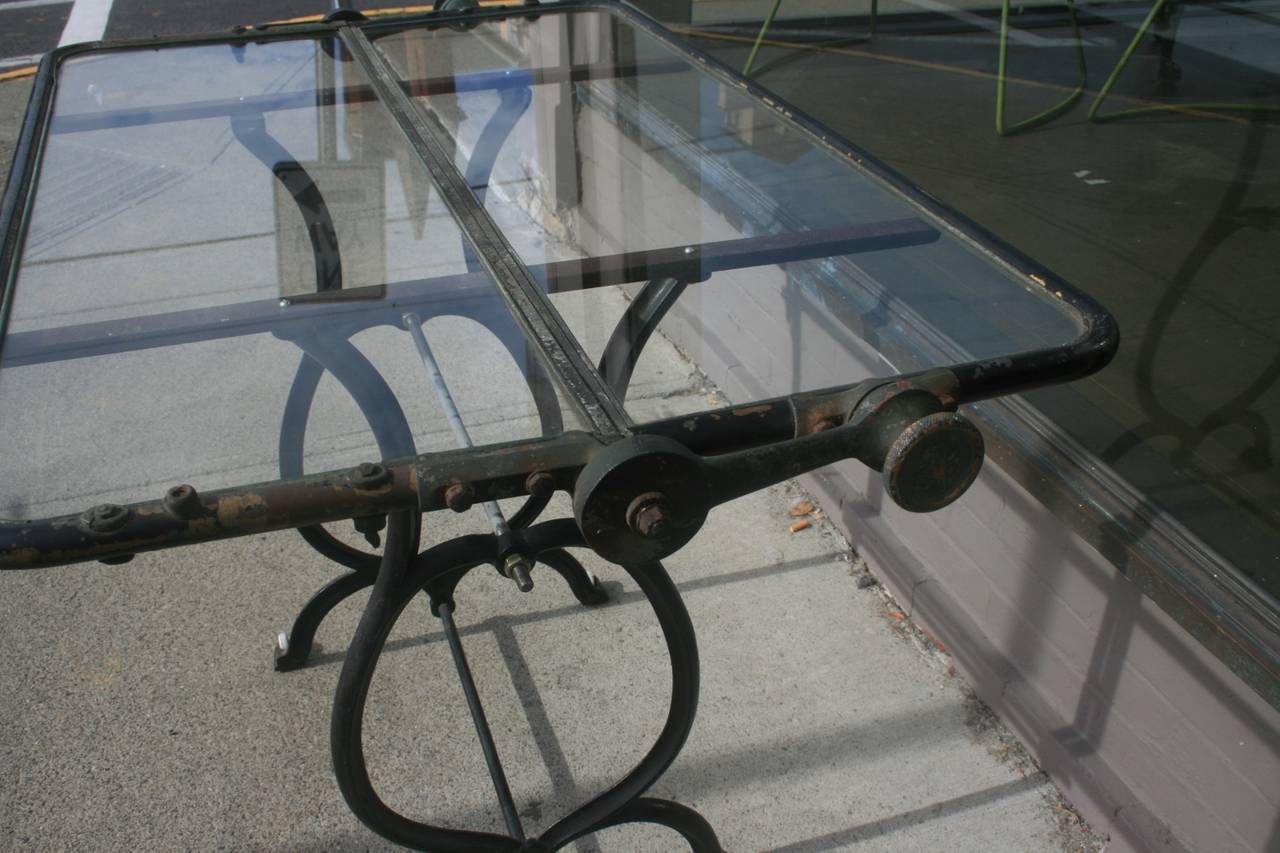 Great old Industrial glass top table. The glass top is thick, encased in a brass, and painted black. It has a wonderful patina and was the windshield from a model T Ford car. The base is cast iron with wheels on one end.