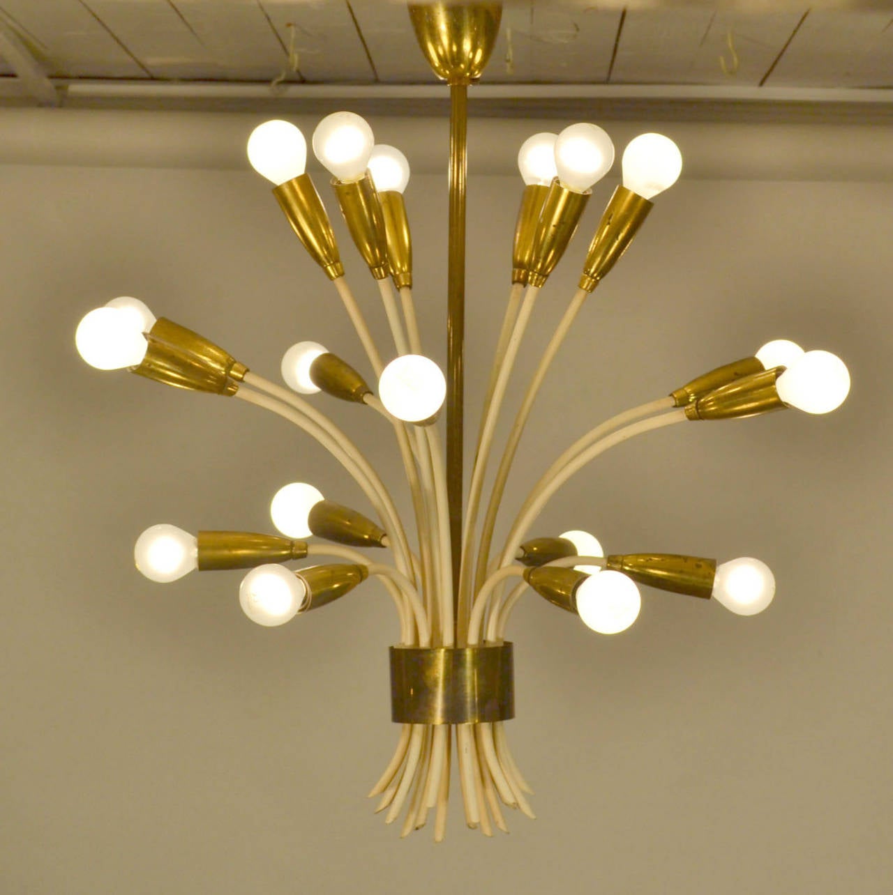 Chandelier in the shape of flowers. An array of 18 individual cream metal stems from around the center is hold together by a ring brass border.