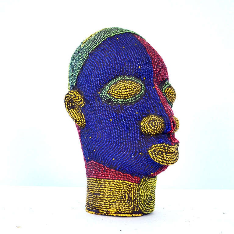 Brightly coloured beaded terracotta head commissioned in the 1960's to decorate wealthy Nigerian homes. The terracotta sculpture is inlaid with strings of beads over its ceramic form.
The artist was influenced by 16th century Benin bronzes.